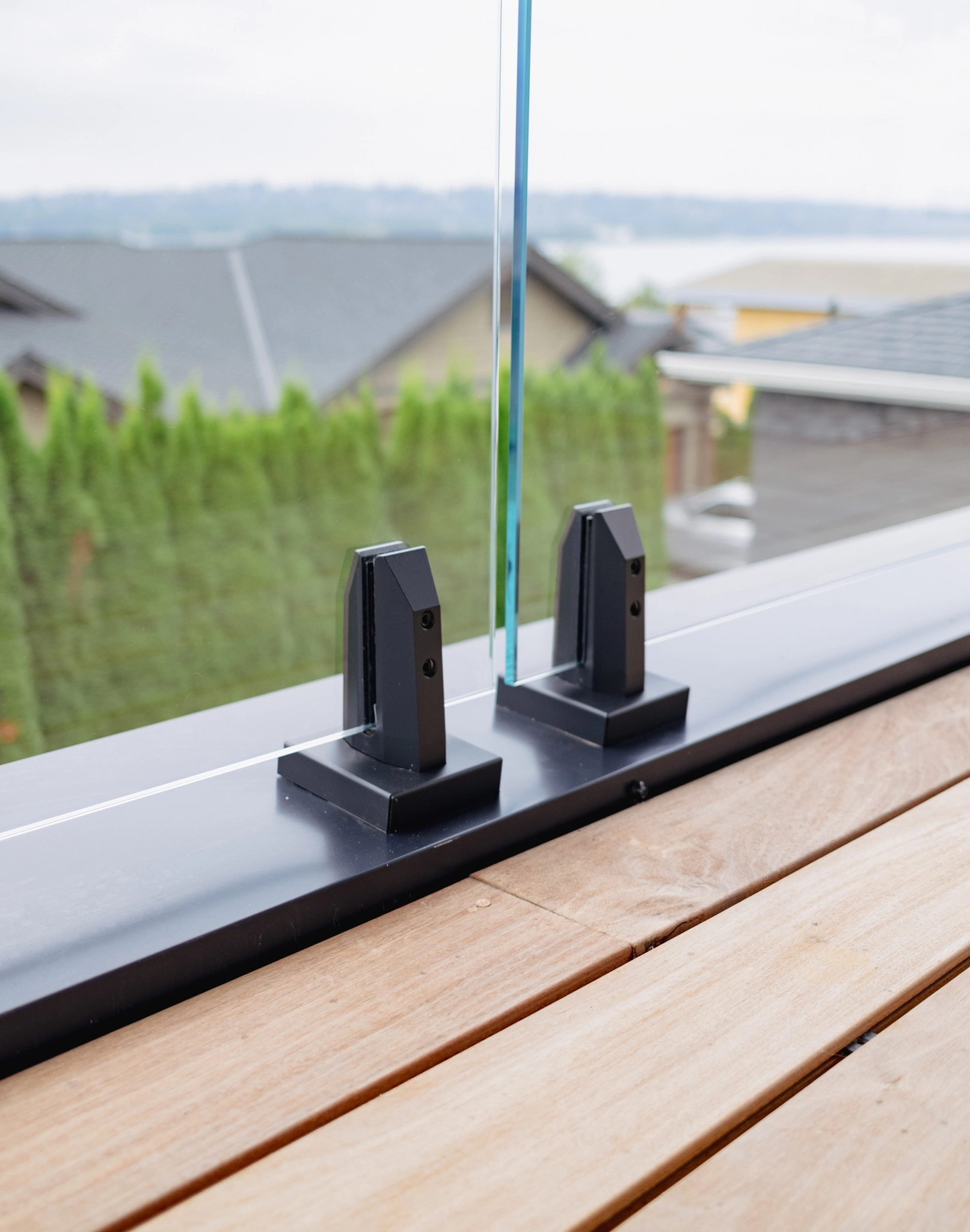 Close-up of two black spigots gripping a glass panel at a deck edge