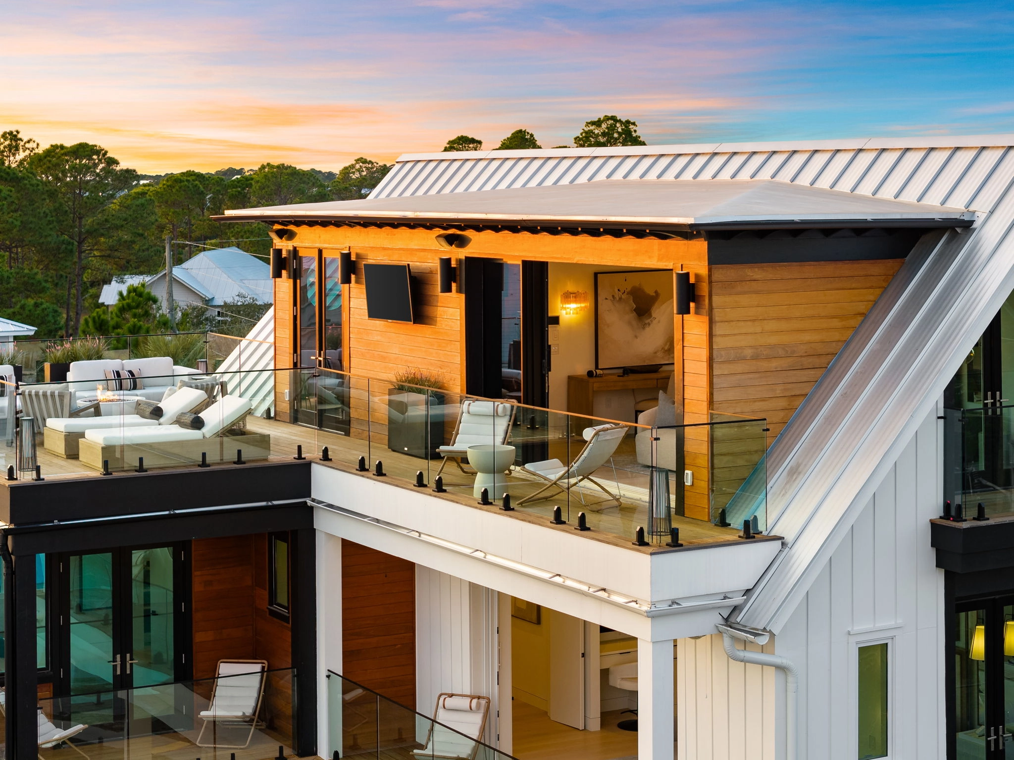 Glass railing wraps an upper balcony glowing warm against a dusk sky