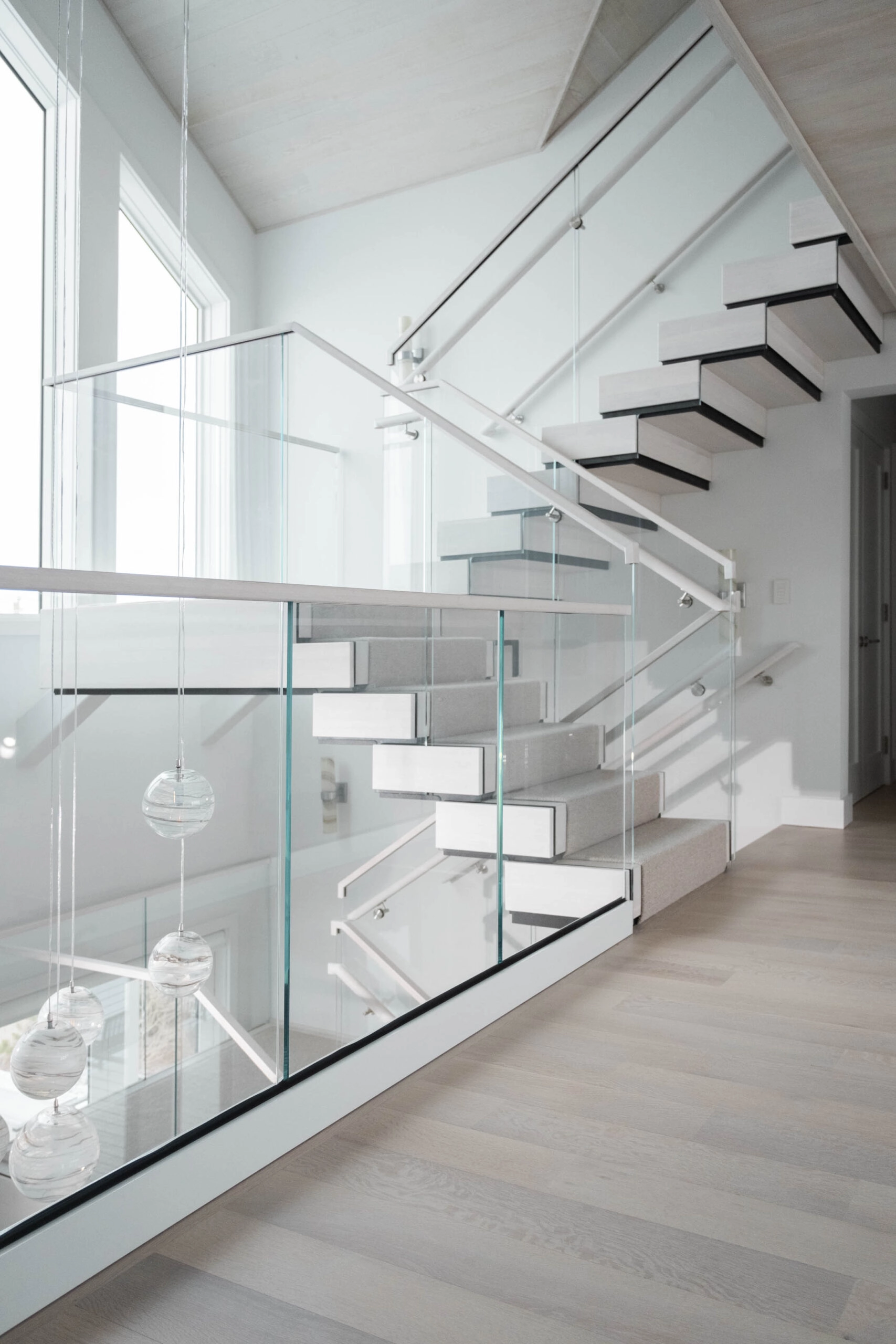 White base rail holds glass panels beside a light-toned floating stair