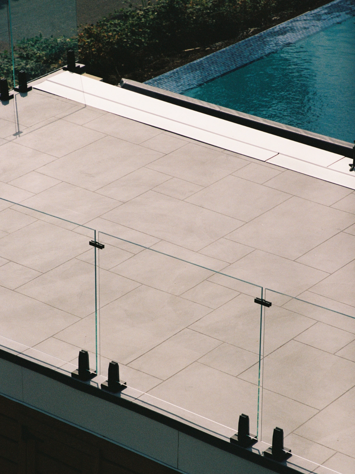 Looking down on a pool terrace where black spigots anchor a glass railing