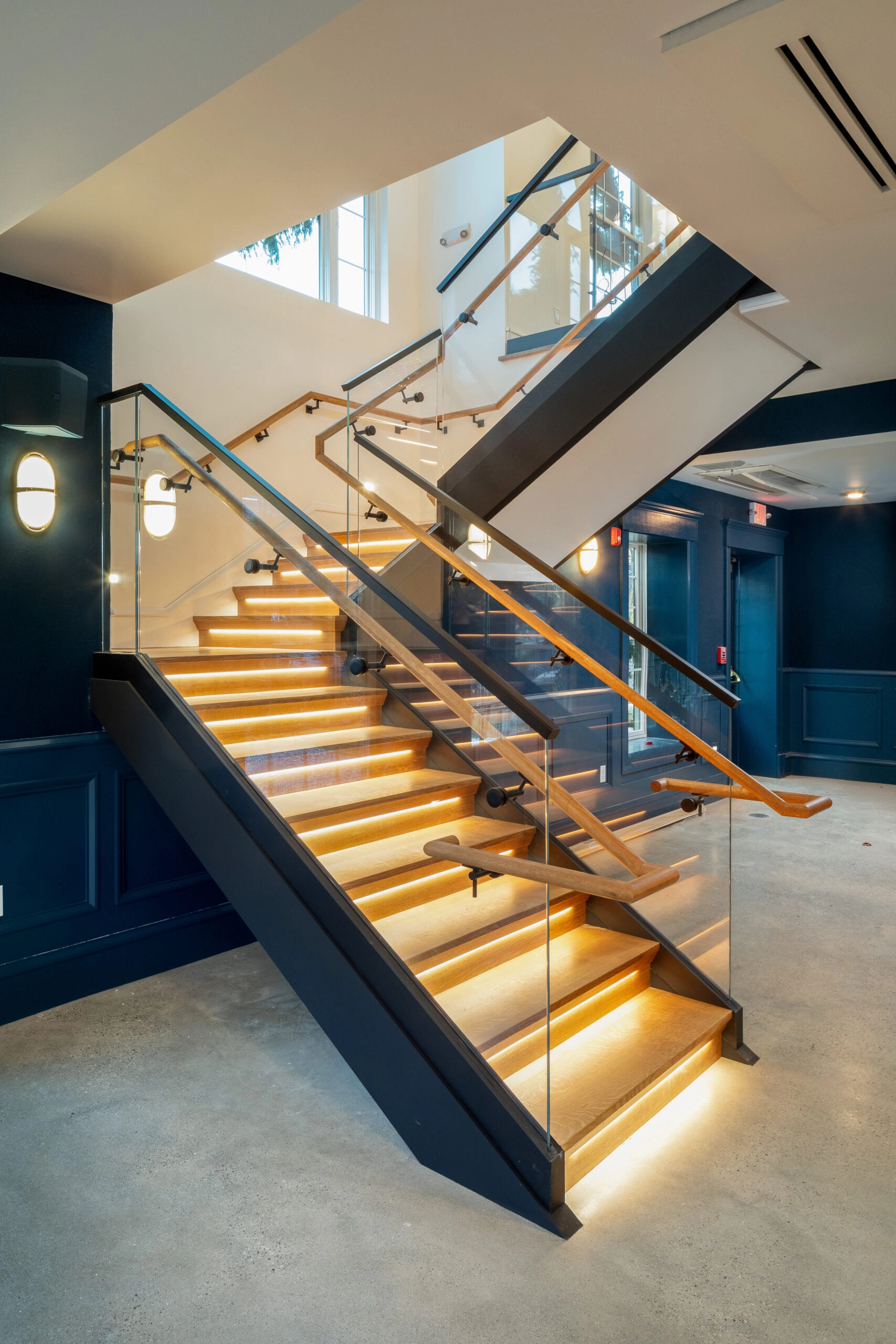 Glass panels seated in a base rail climb a stair lit from beneath each tread