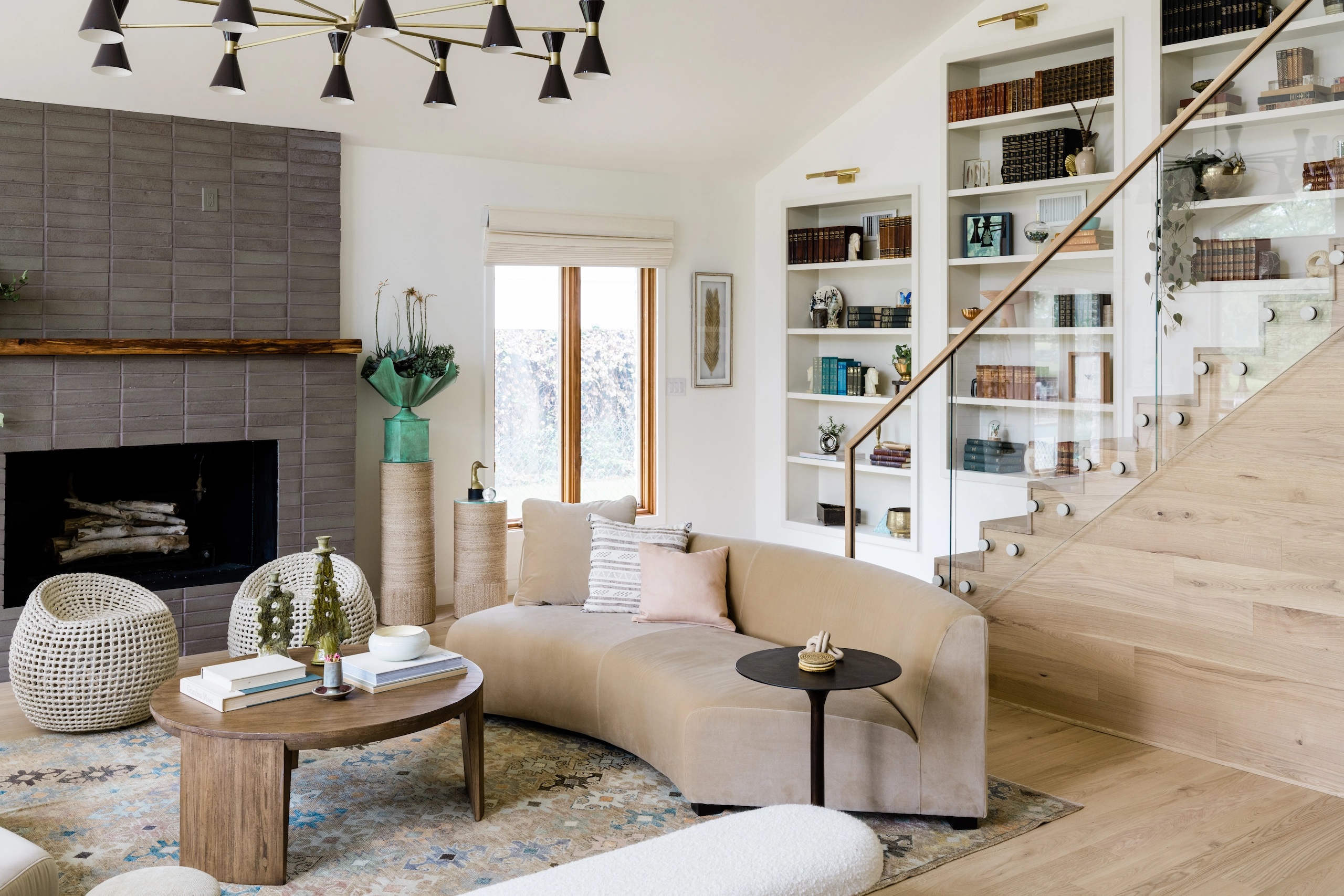 A glass railing with wood handrail borders a living room lined with bookshelves