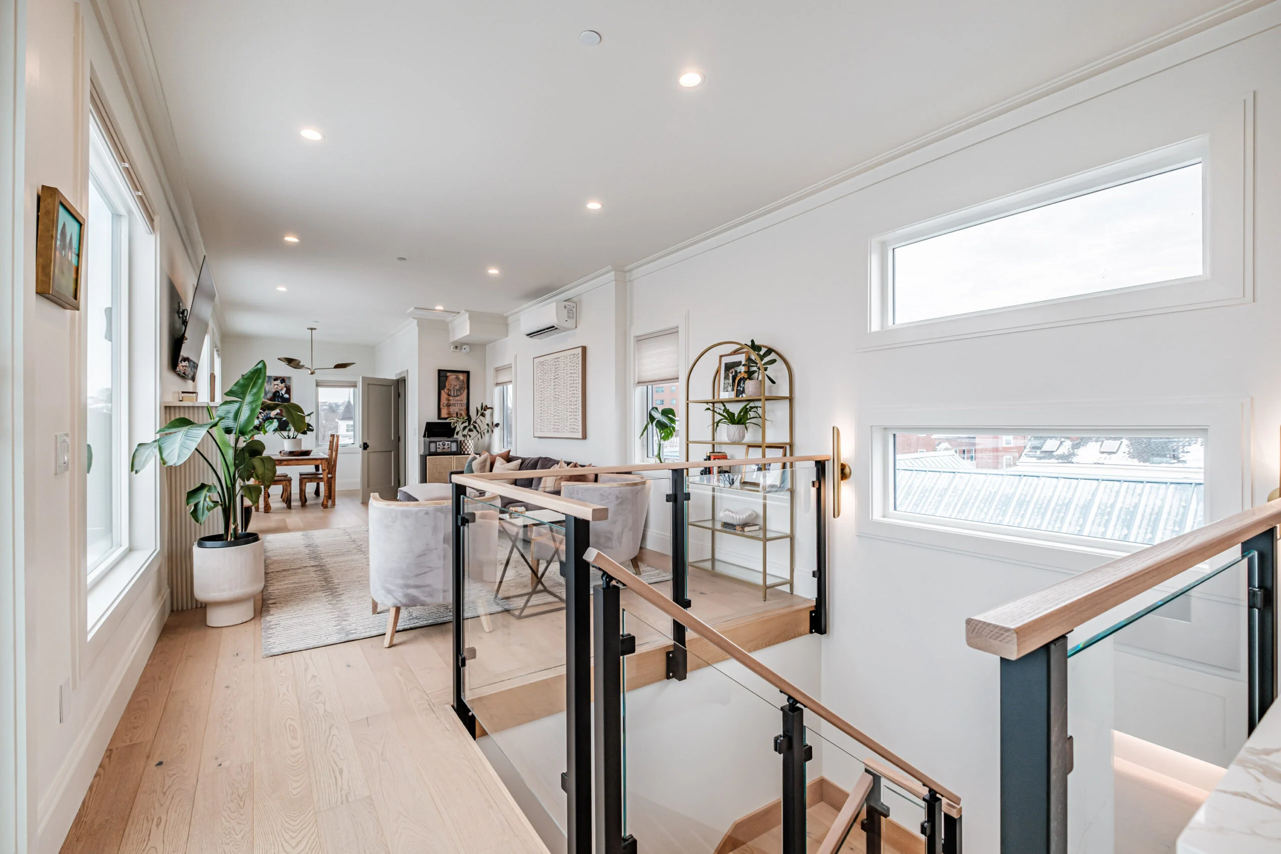 Wood-capped glass railing overlooks a living area from an upper landing