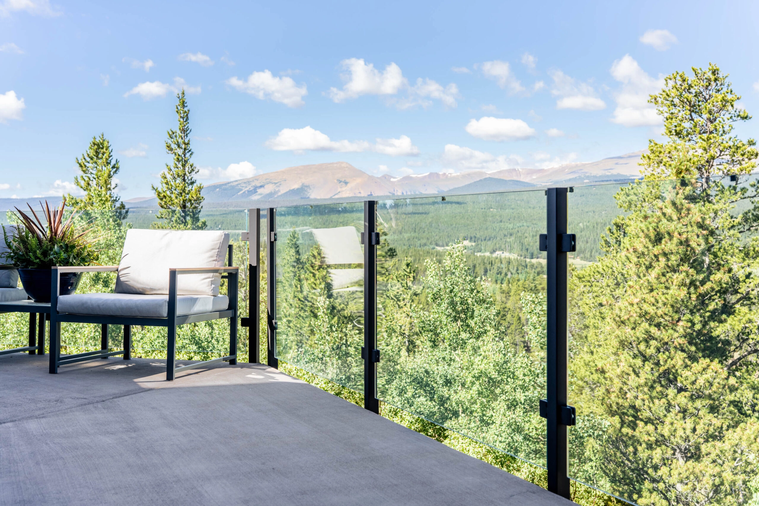 Post-mounted glass railing wraps a mountain deck with a pair of lounge chairs