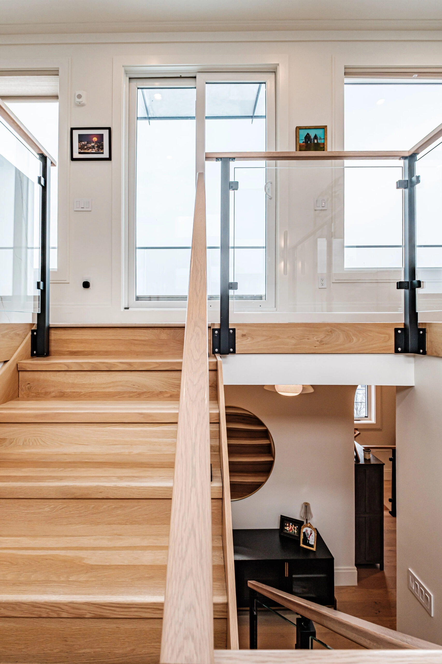 A stairwell framed by glass panels in black posts opens to bright windows