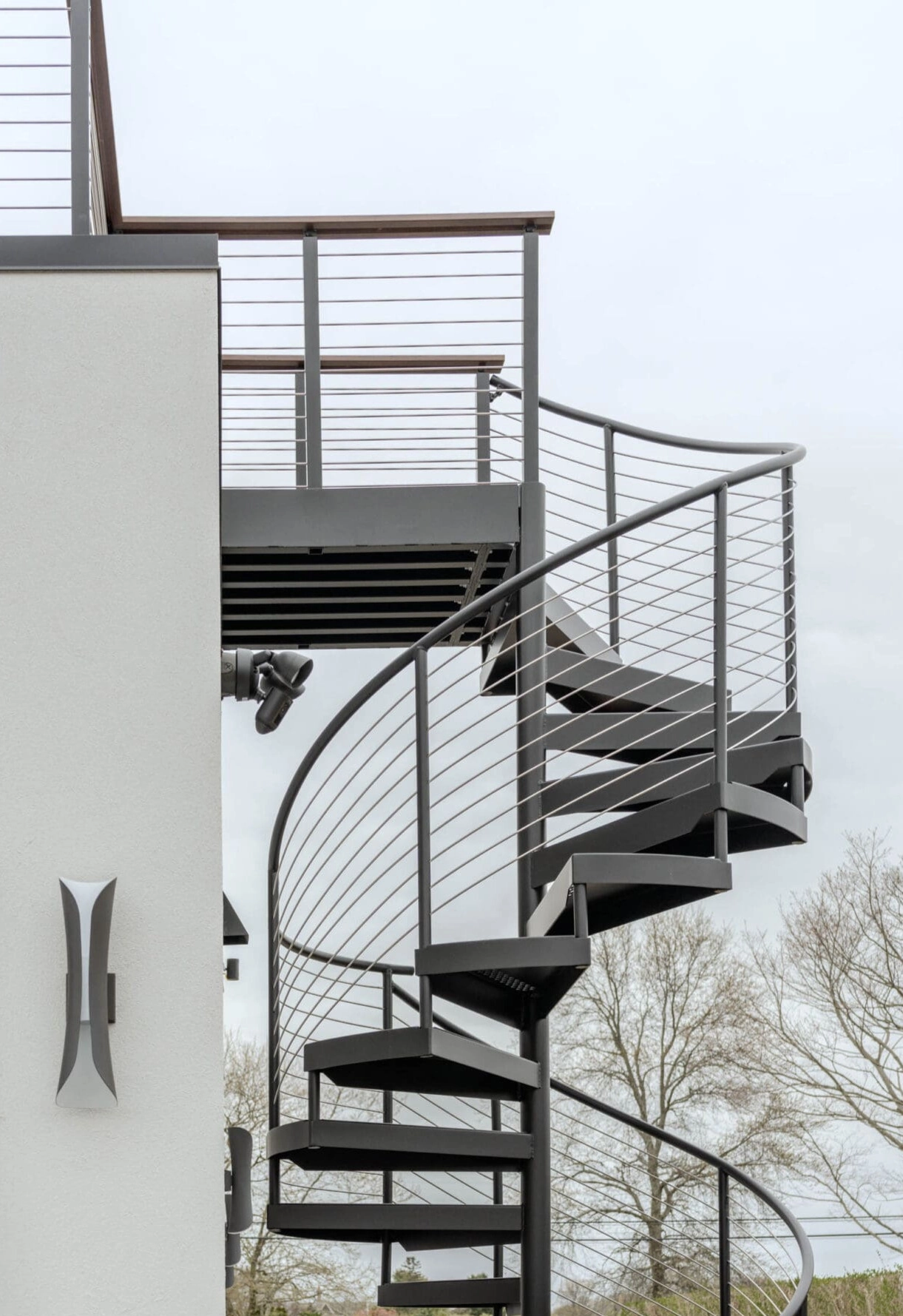 An exterior spiral stair with cable railing drops from a rooftop deck