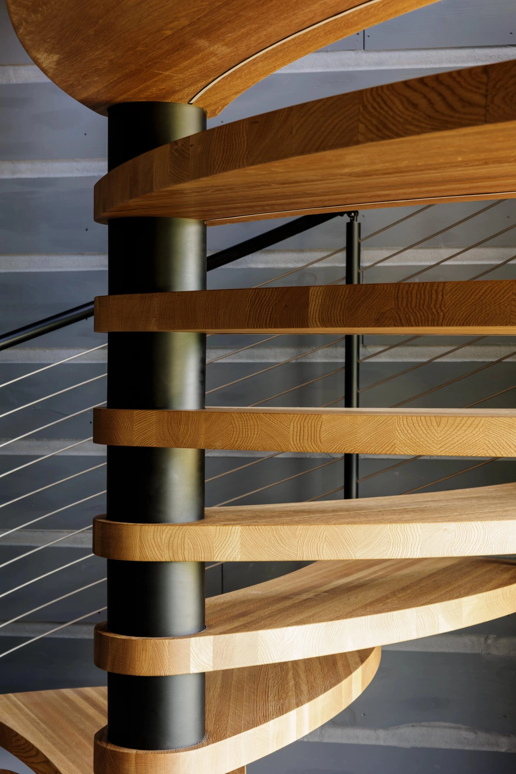 Wood treads radiate from a spiral stair's center column behind cable infill