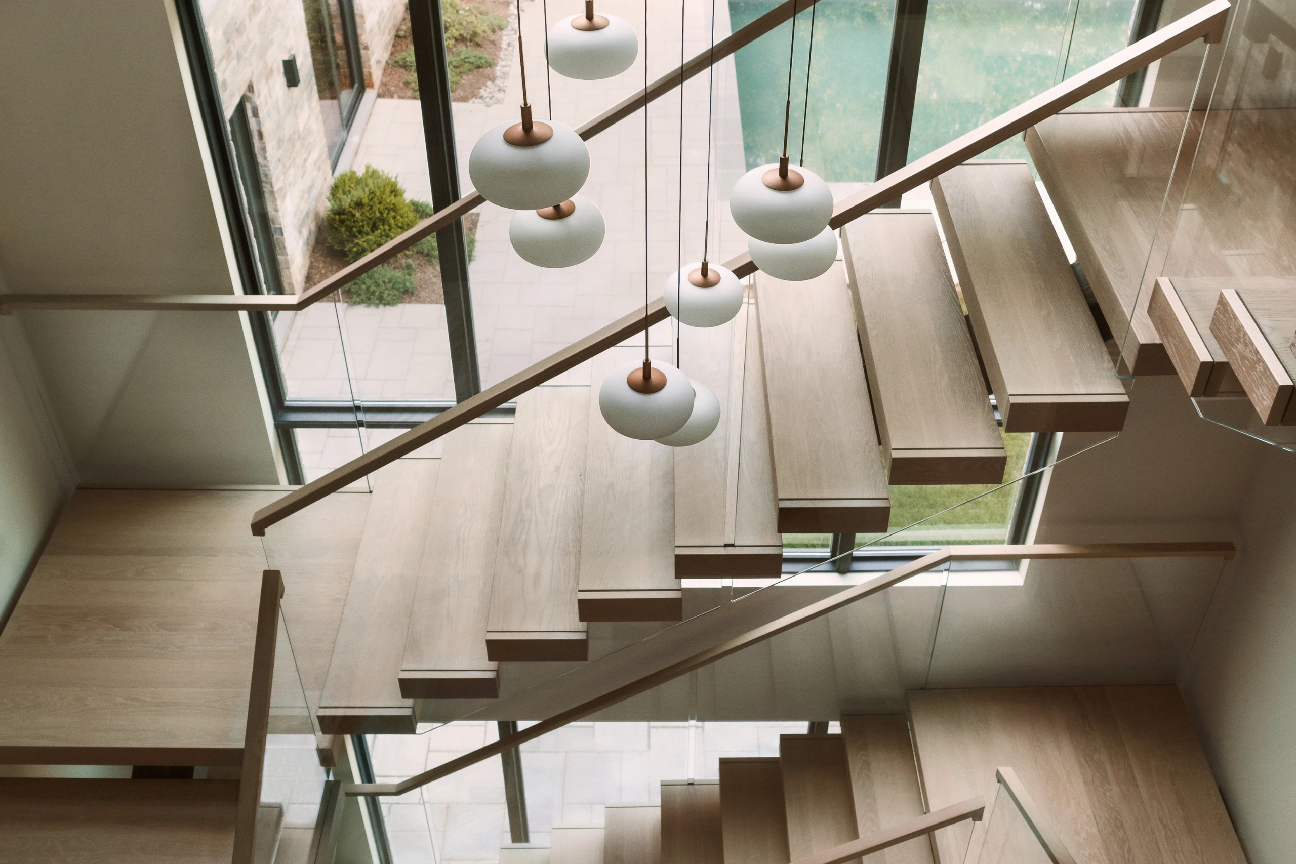 Two flights climb behind glass railing under a cluster of globe pendants