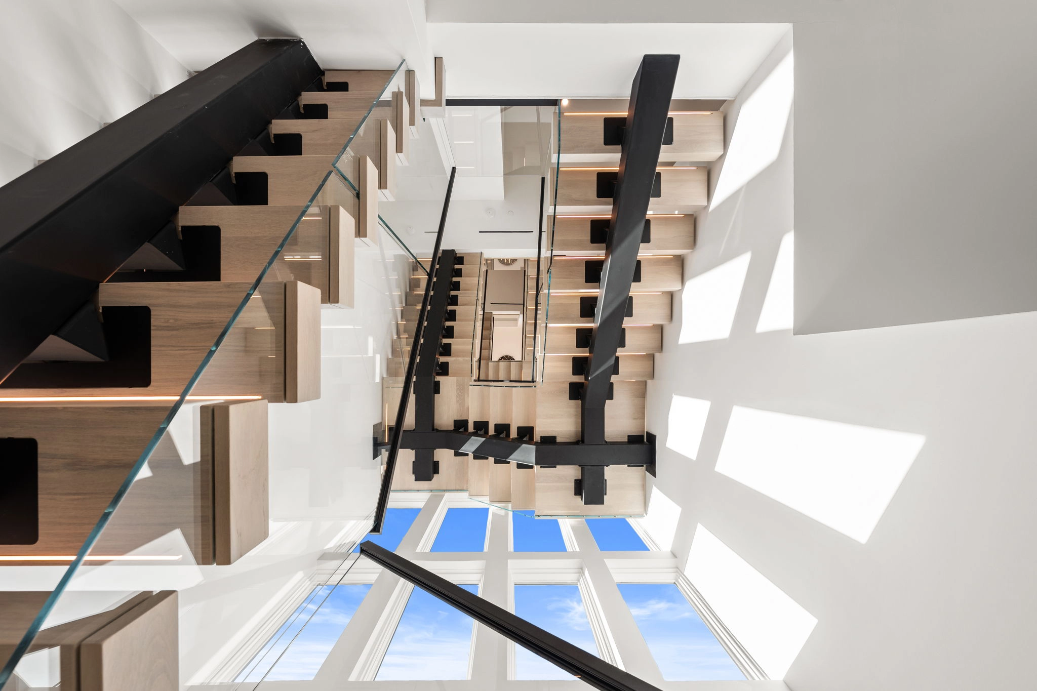 Looking up a multi-level stairwell where a black stringer carries pale treads
