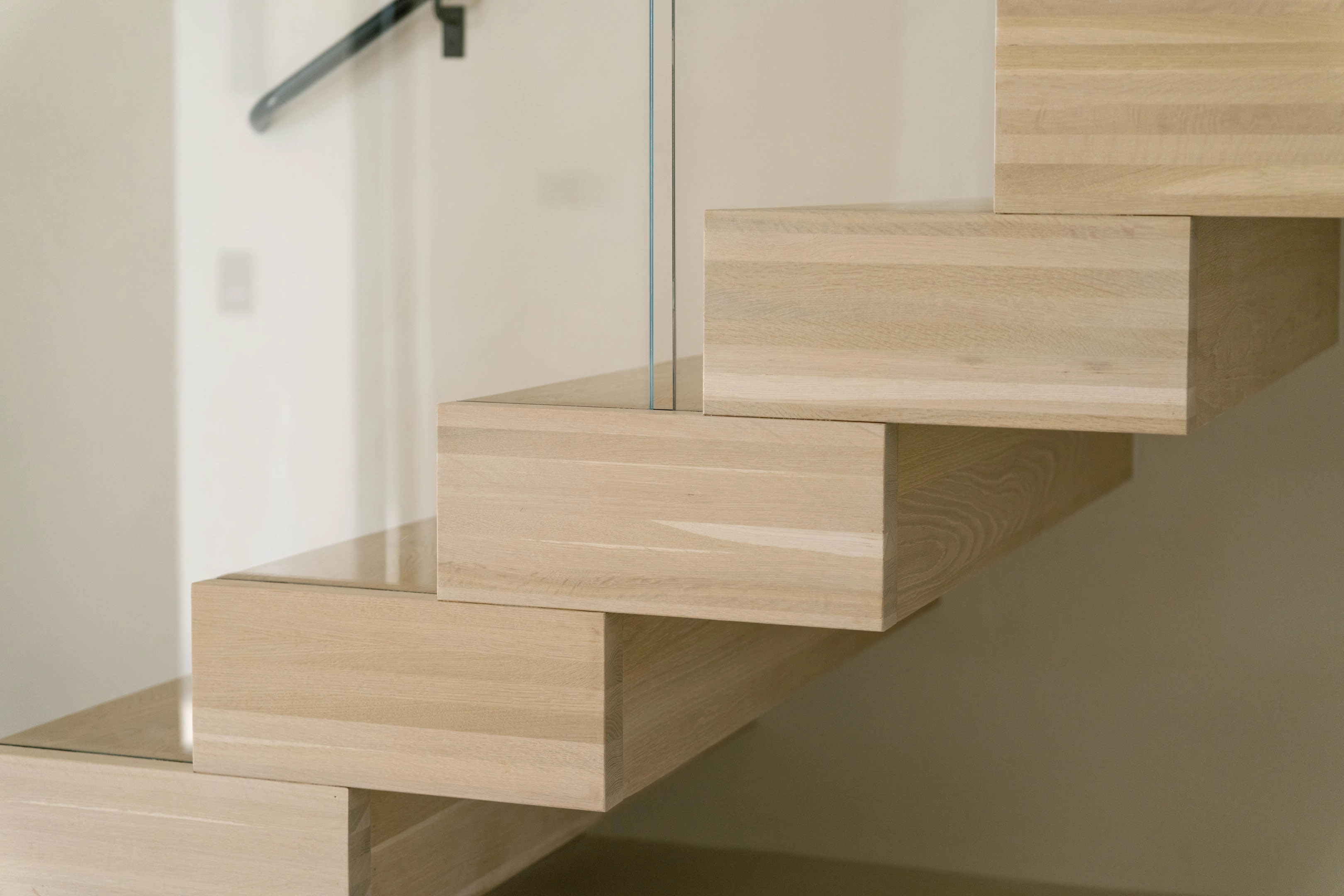 Close-up of stacked wood box treads meeting a frameless glass railing