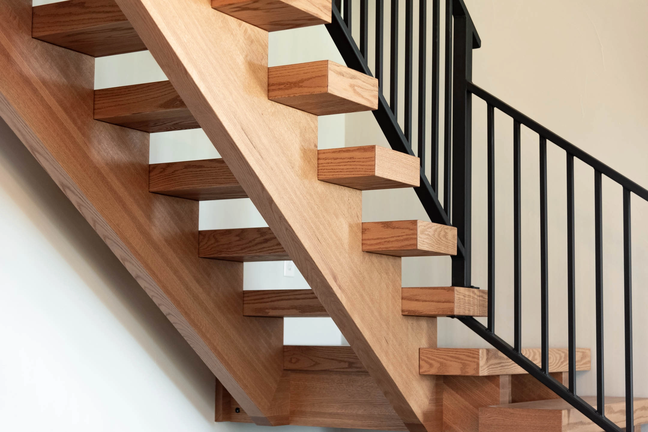 Wooden duo stringers carry box treads behind a run of slim black balusters