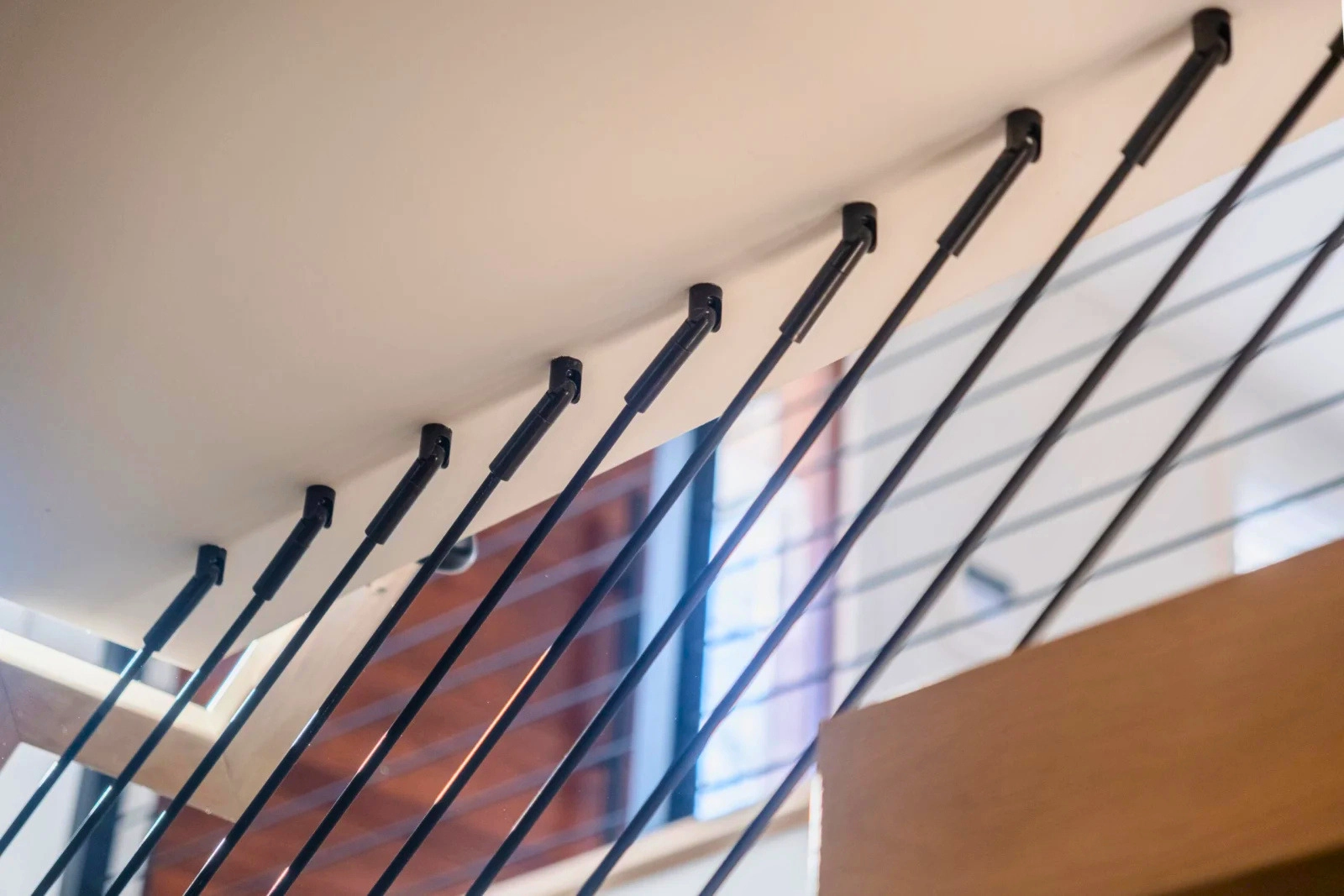 Black rods angle into an overhead header along a stair in a white interior