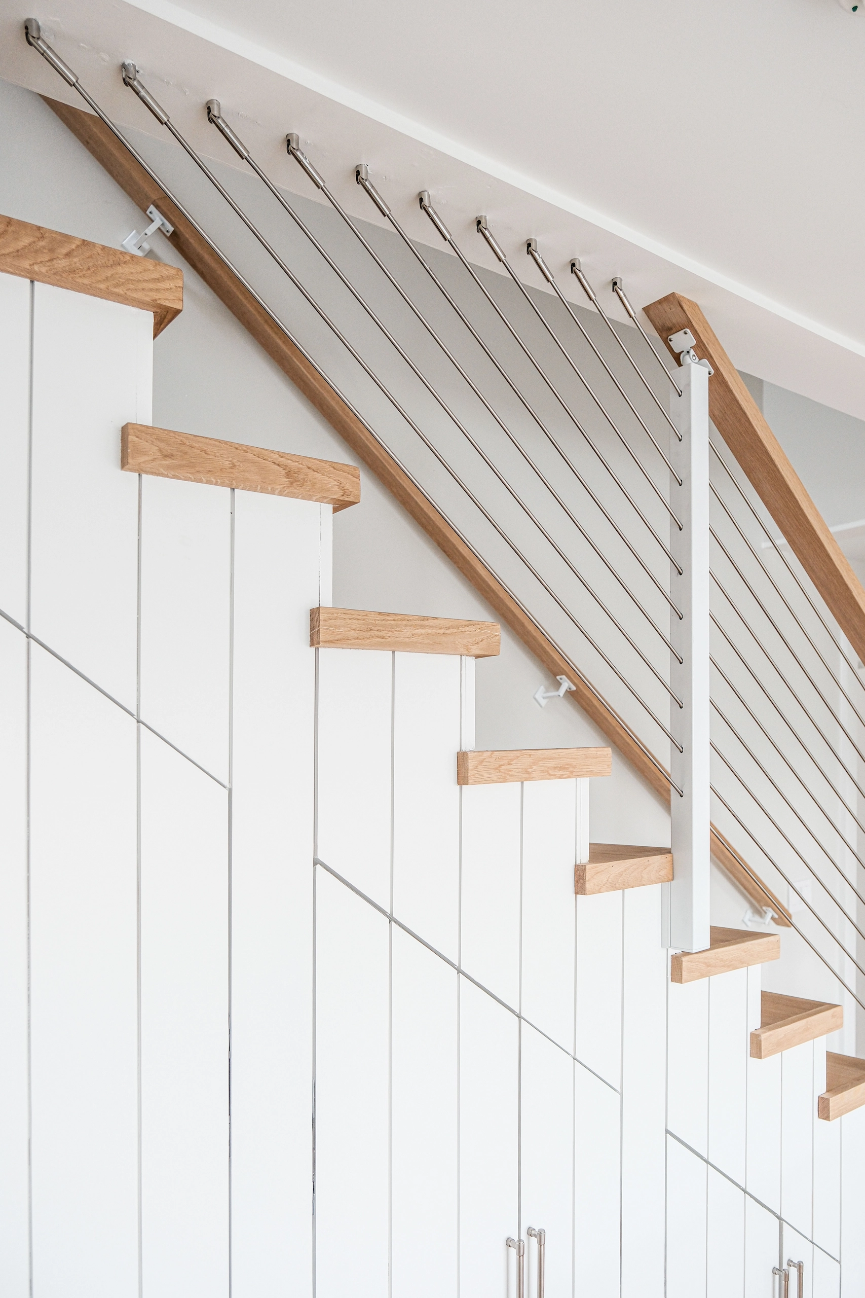 White side-mounted posts carry rod infill up a staircase with wood treads