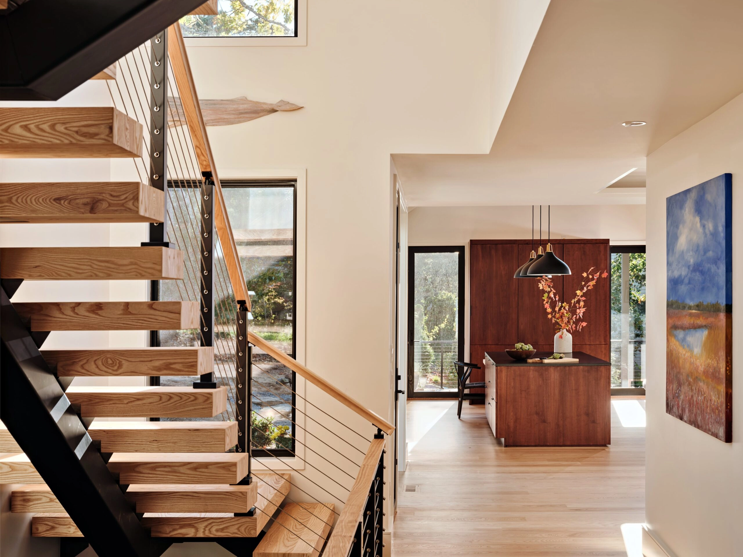 Cable railing with a wood handrail climbs beside an open kitchen and dining nook