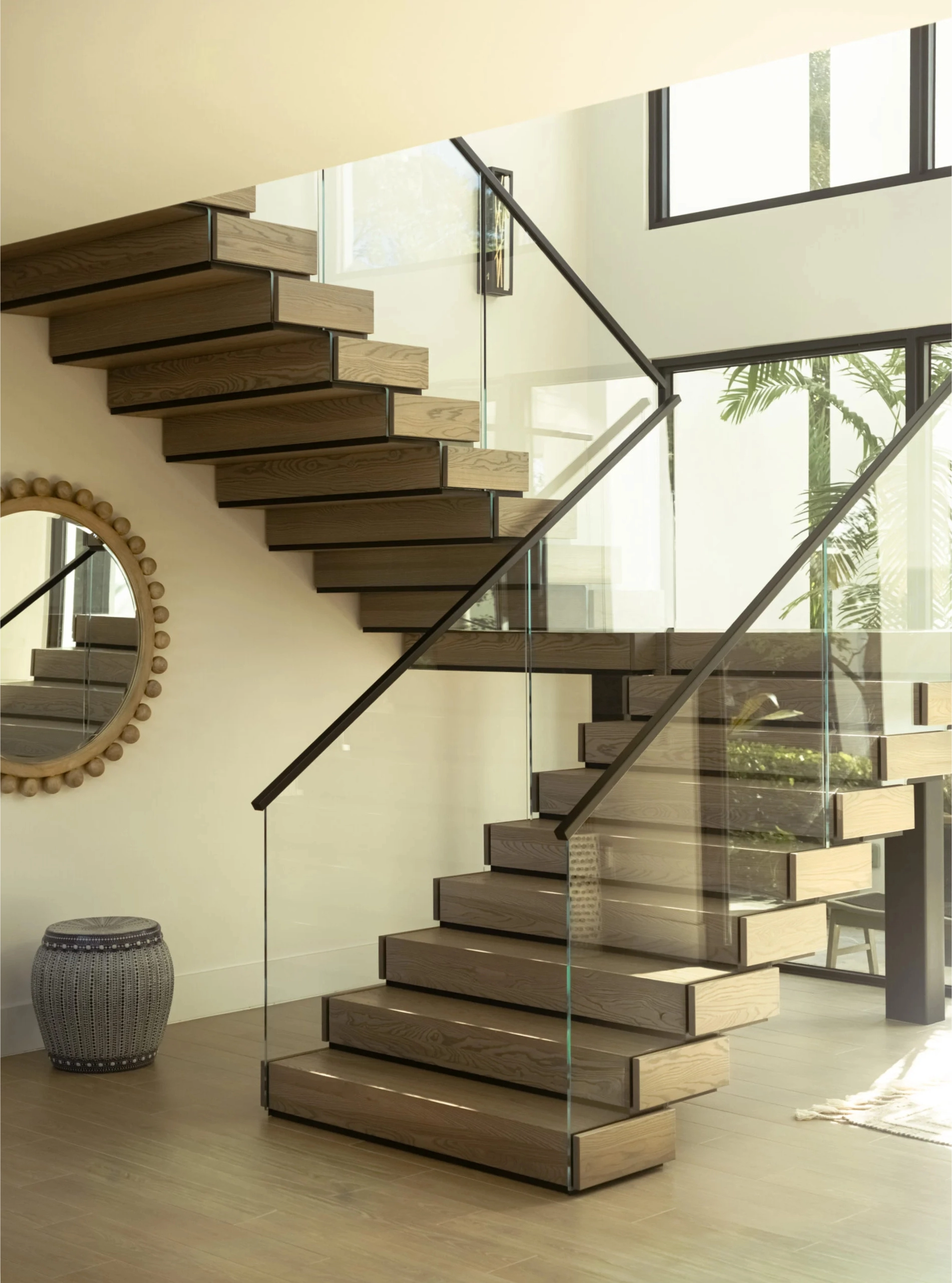 Stacked treads rise behind a glass panel past a woven round wall mirror