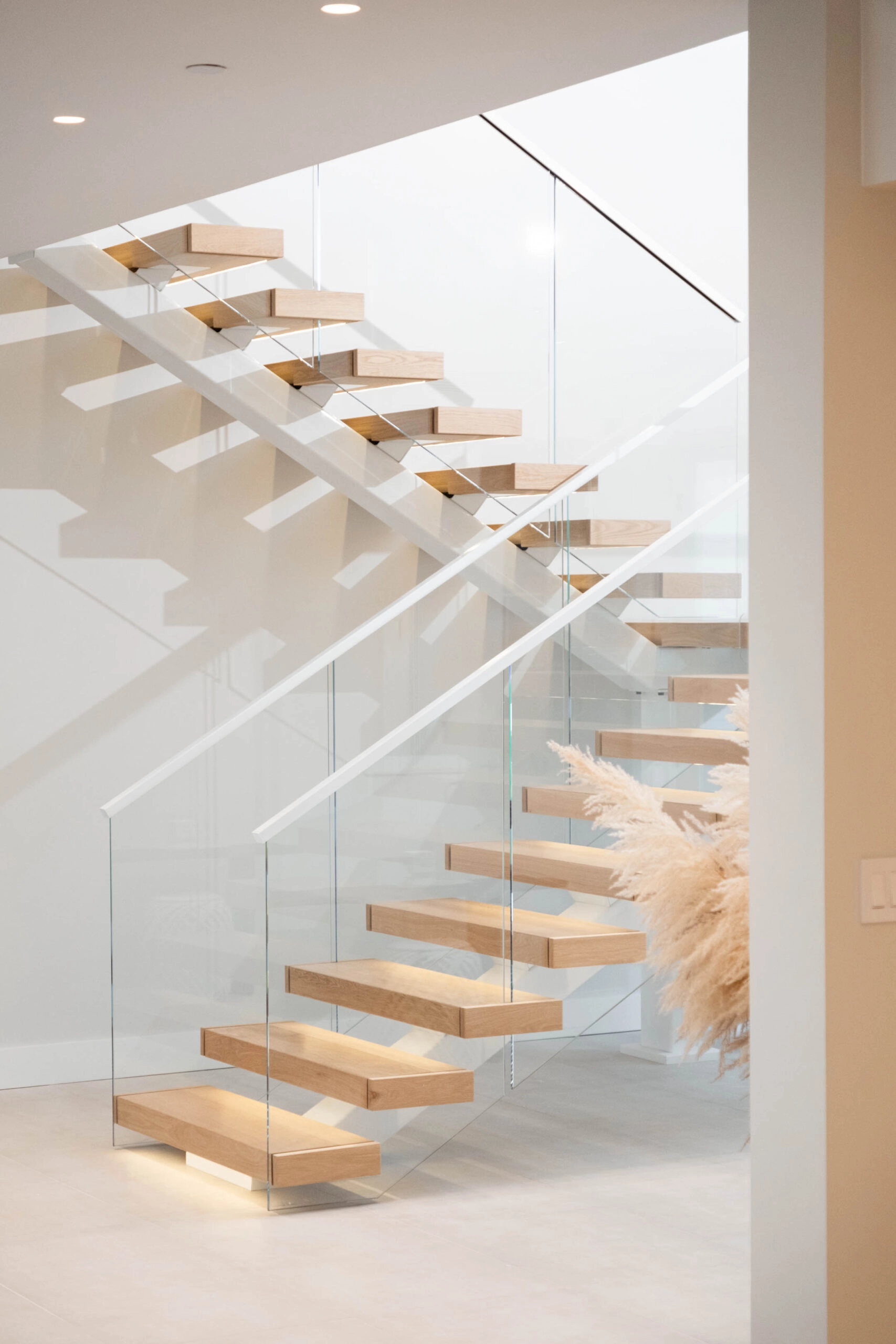 White stringers and wood treads zigzag up behind full-height glass panels