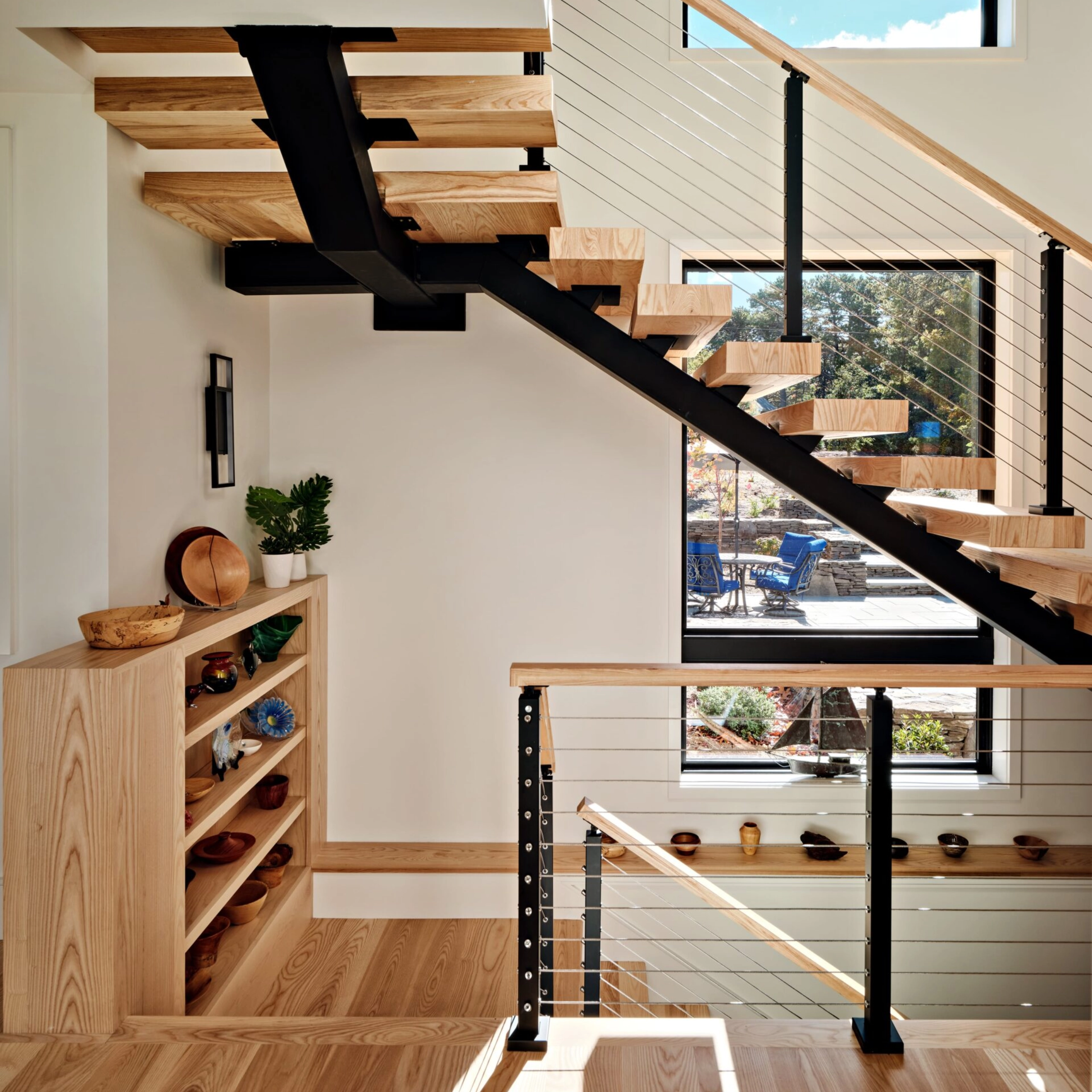 A wood handrail and cable infill pass a built-in shelf and plank wall