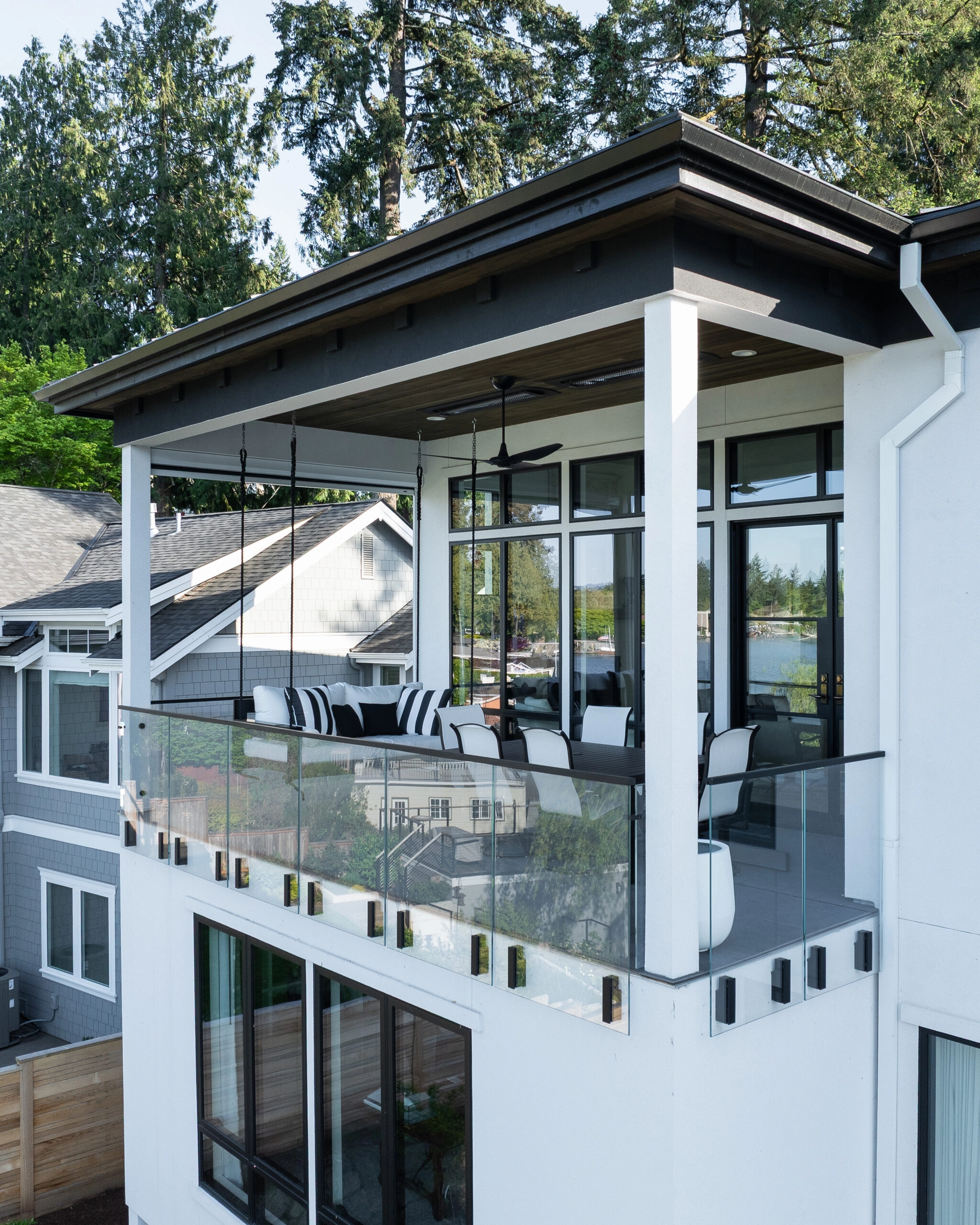 Glass balcony railings stack across a white lakeside home among tall firs