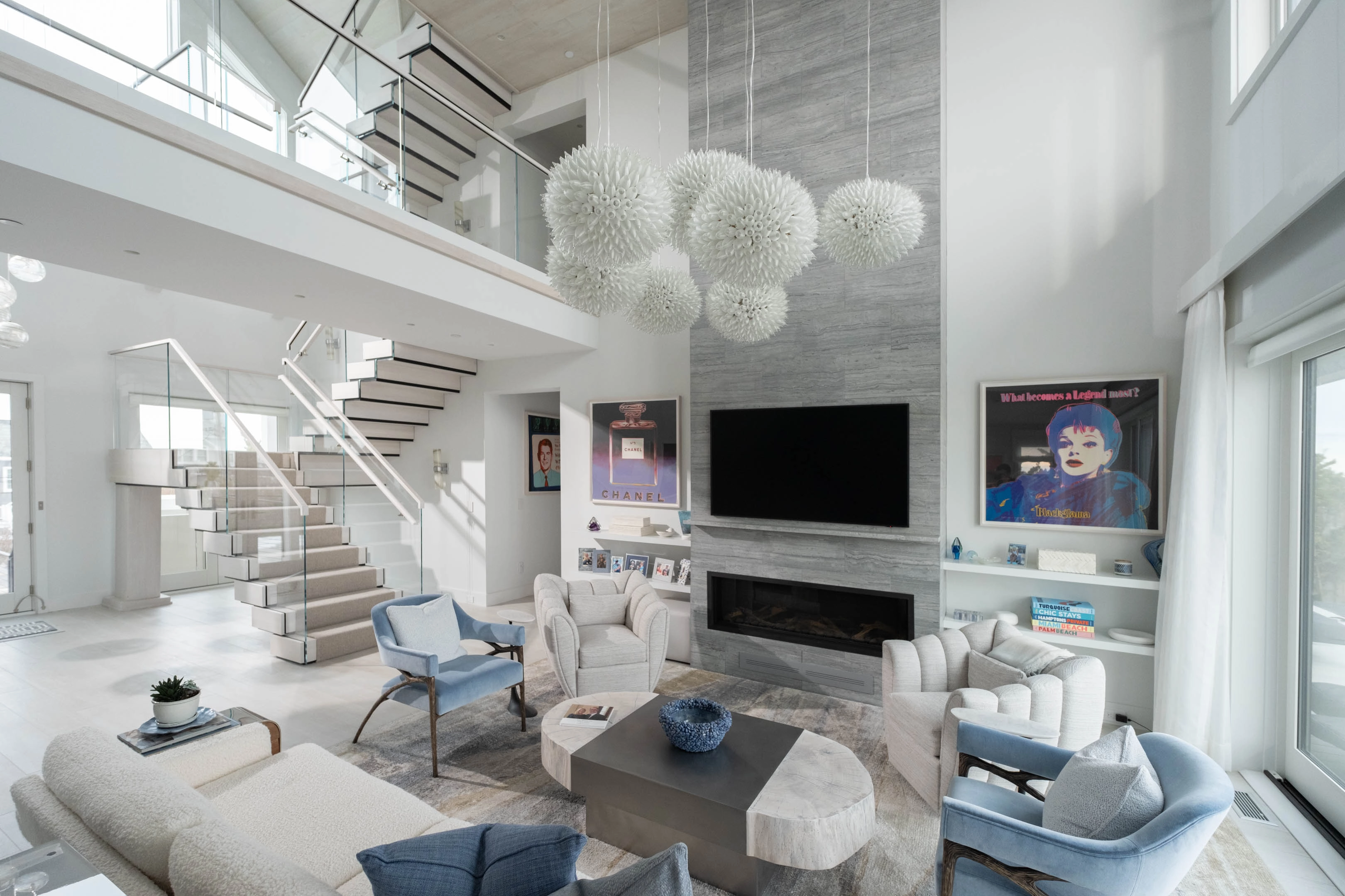 A stacked stair with glass railing rises above a bright double-height living room