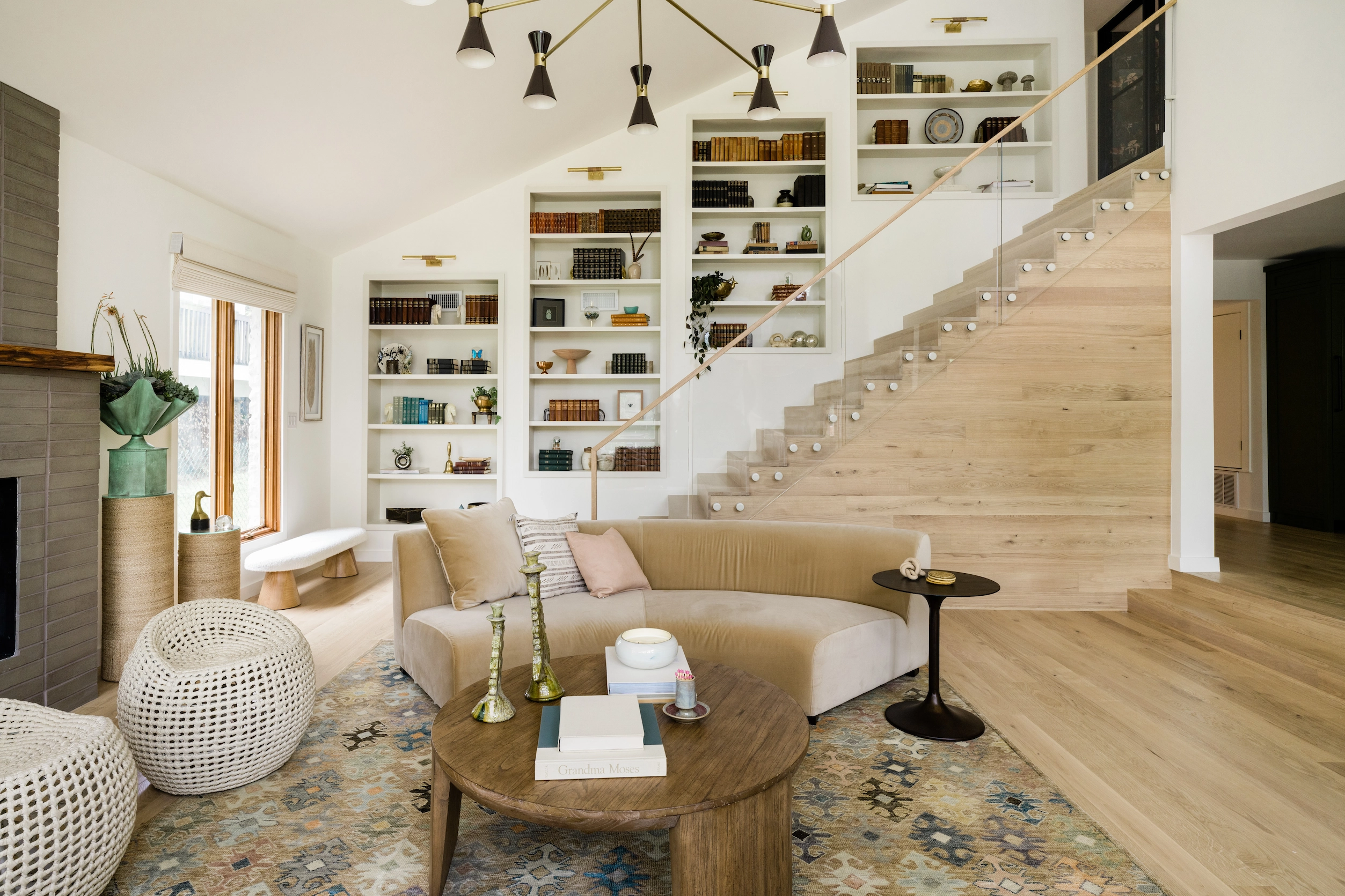 Glass railing borders a stair above a living room lined with open shelving