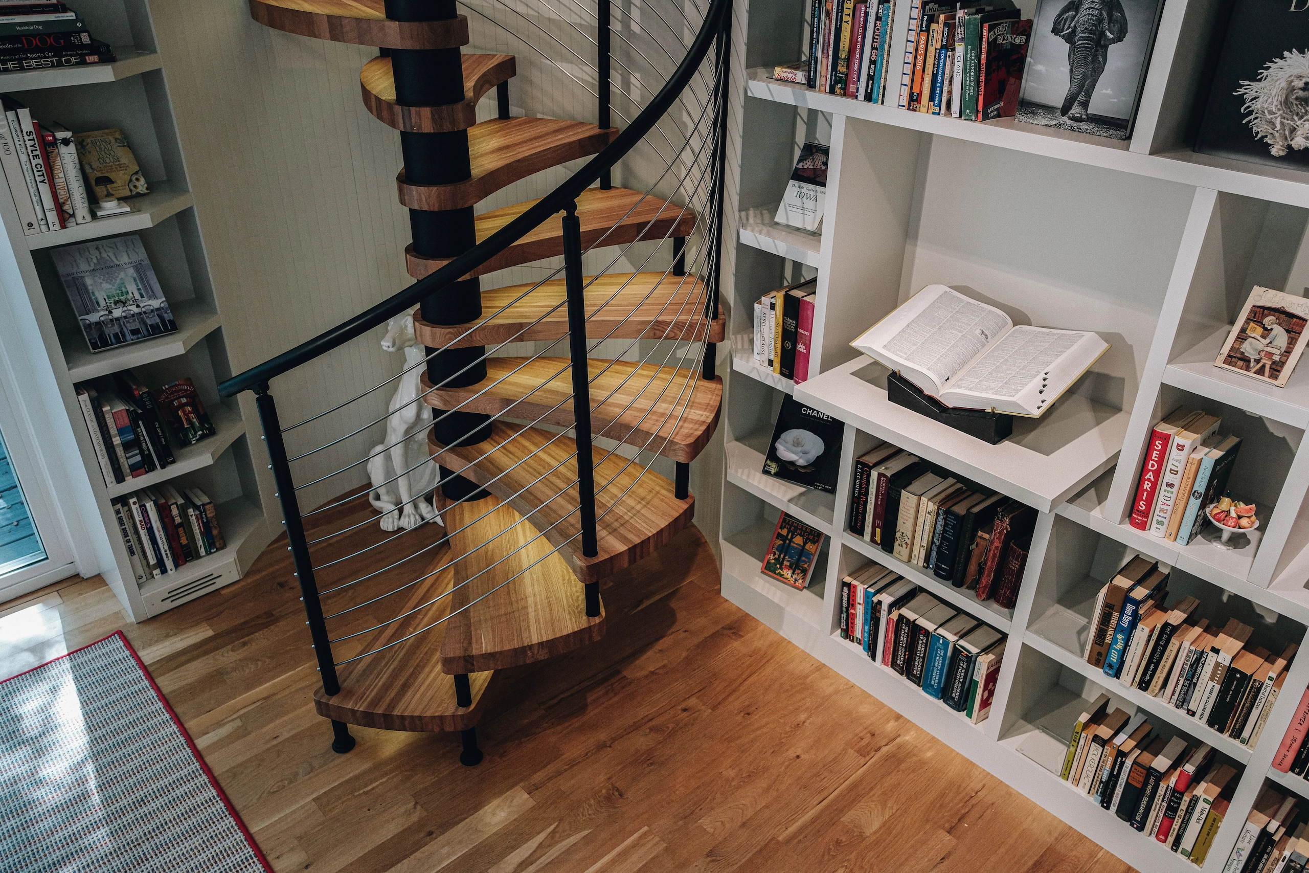 A spiral stair turns between white bookshelves on a warm wood floor