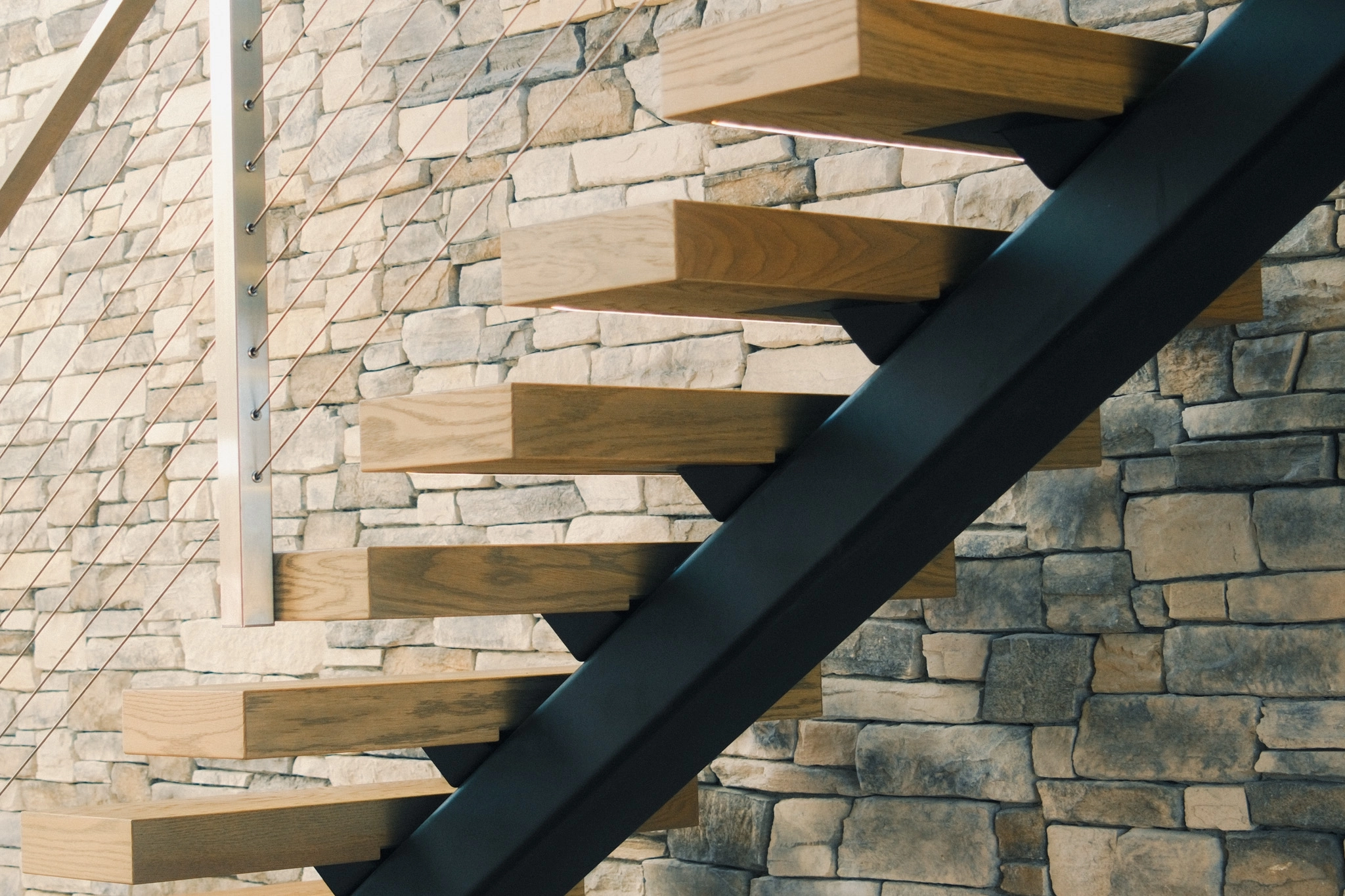 Cable infill and a black stringer carry wood treads up a stacked stone wall