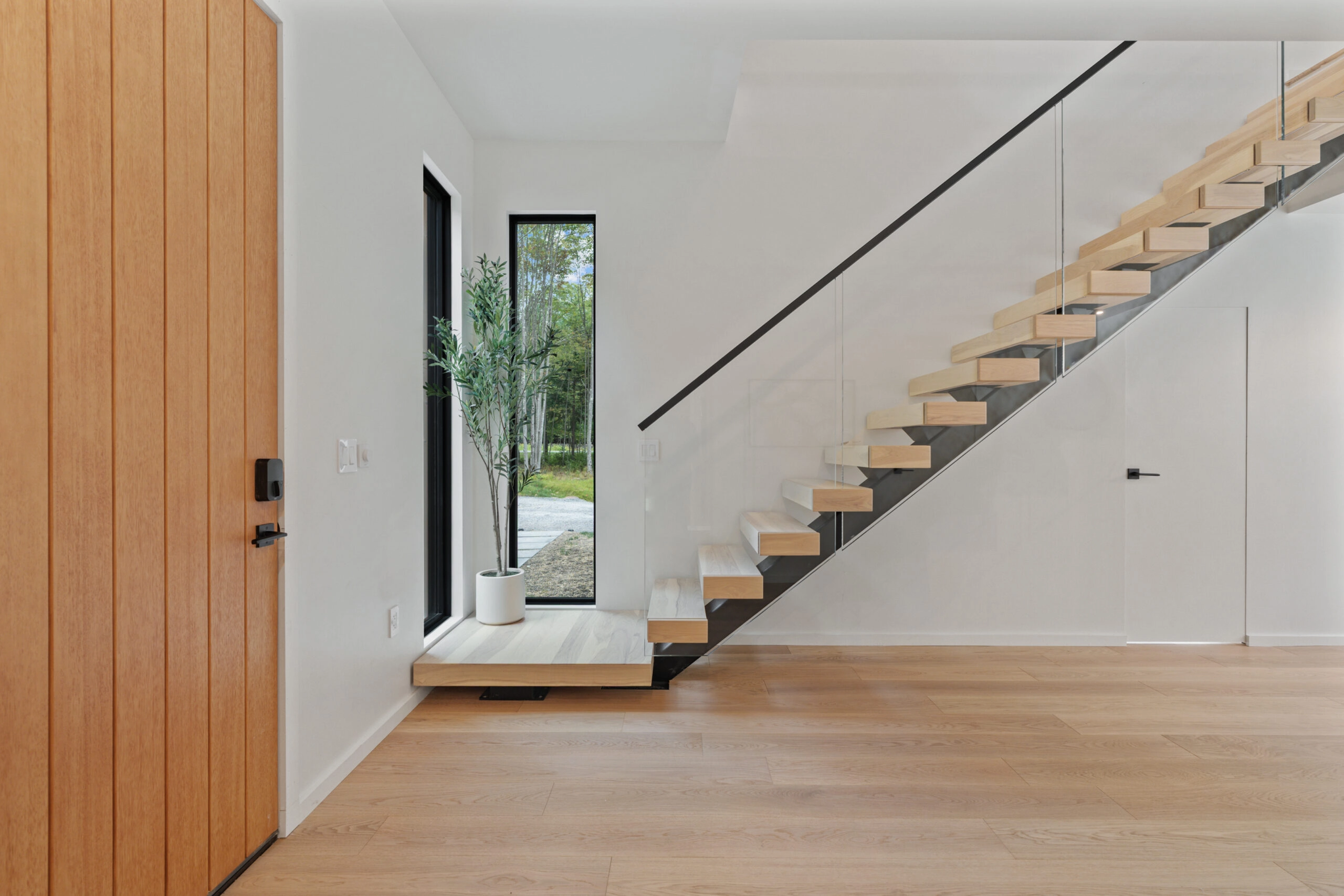 A floating stair sits past a wood door in a bright and spare hallway