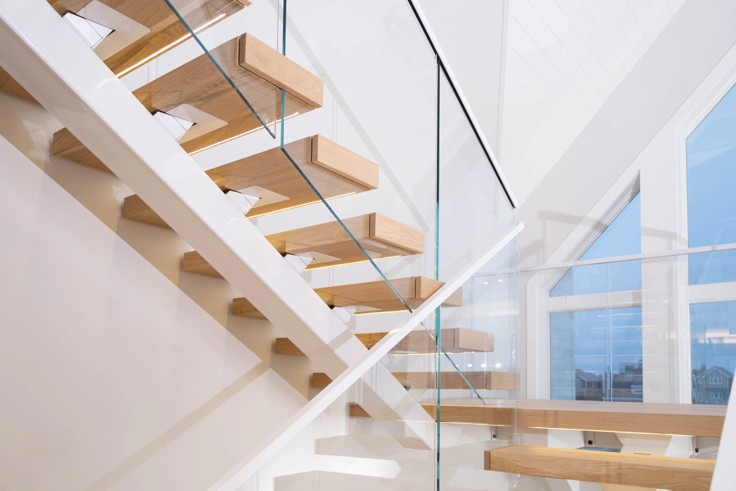 Lit treads and glass panels stack through three floors of a white stairwell