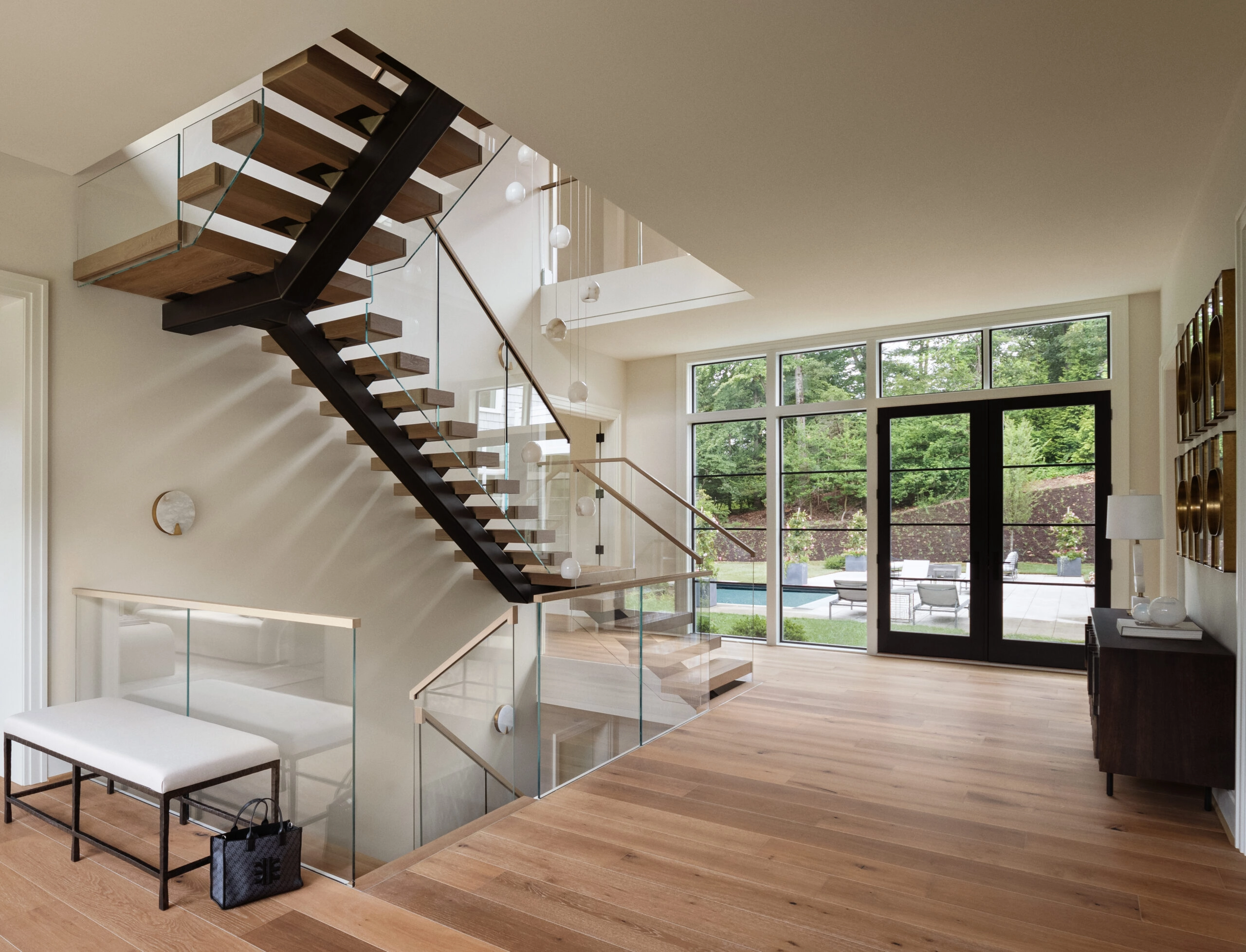 A switchback floating stair with glass railing anchors a window-lined room