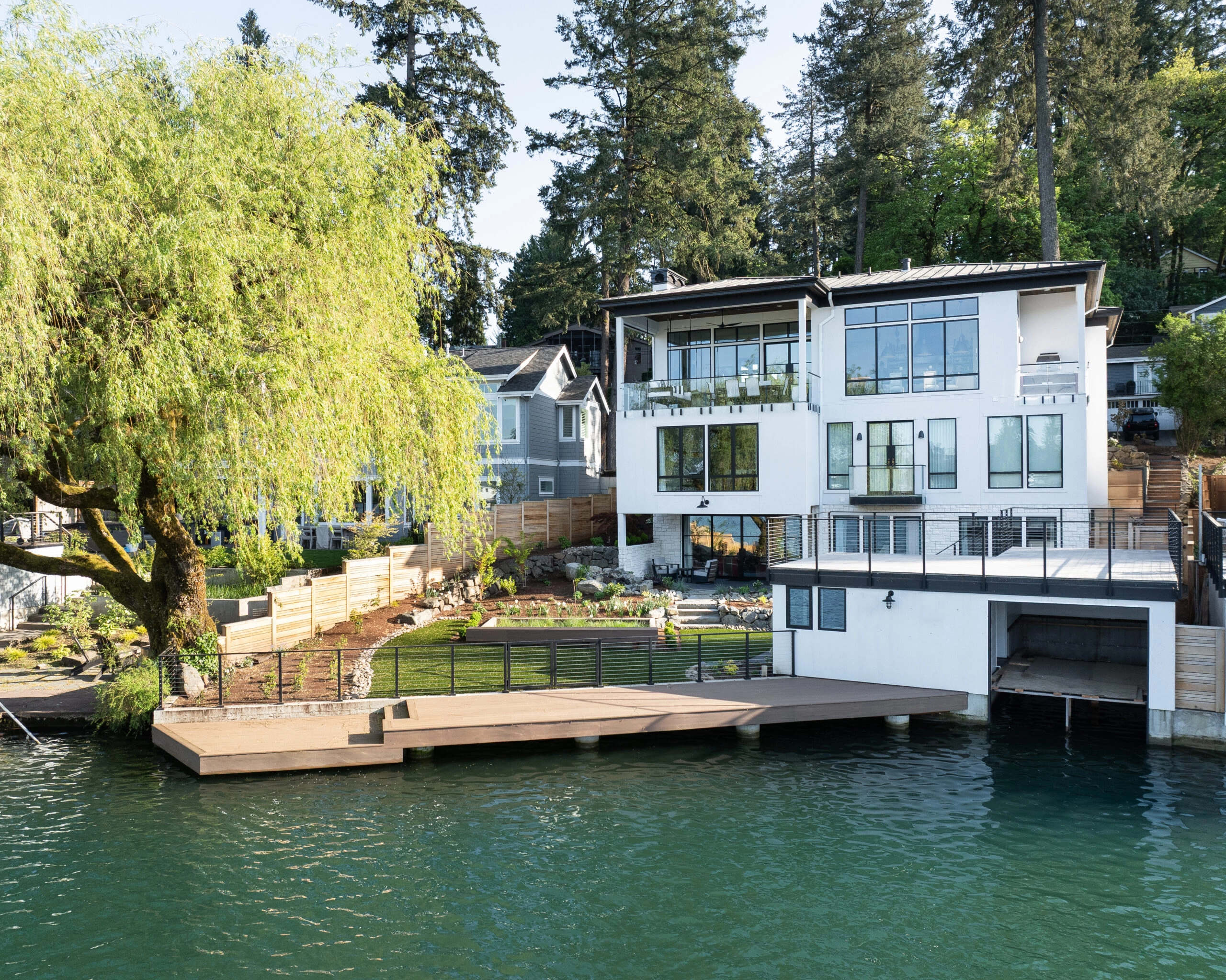 A lakeside house shows side-mounted glass railings across its decks and dock