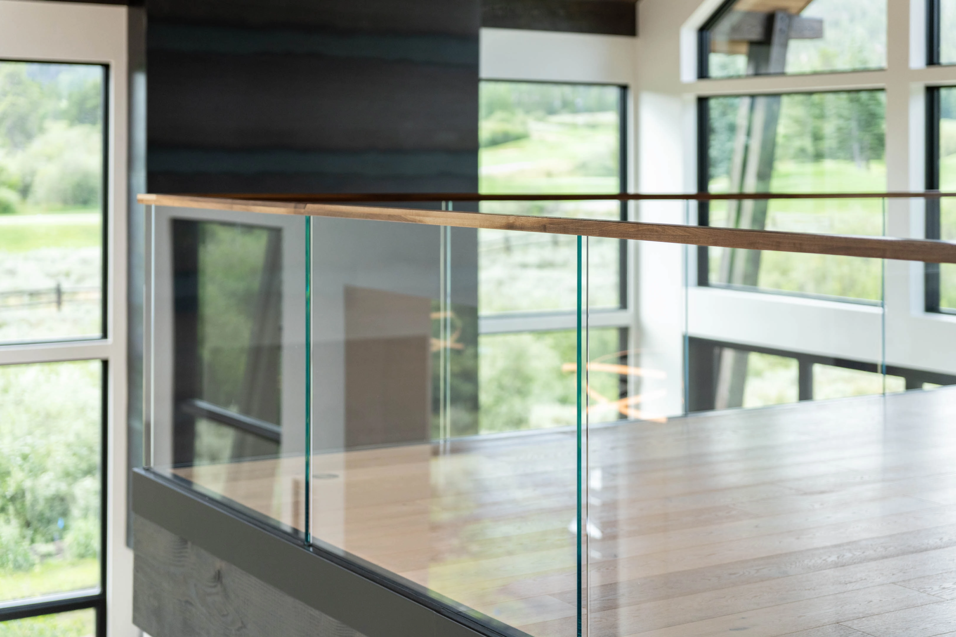 Wood-topped glass railing rings a loft opening framed by tall windows