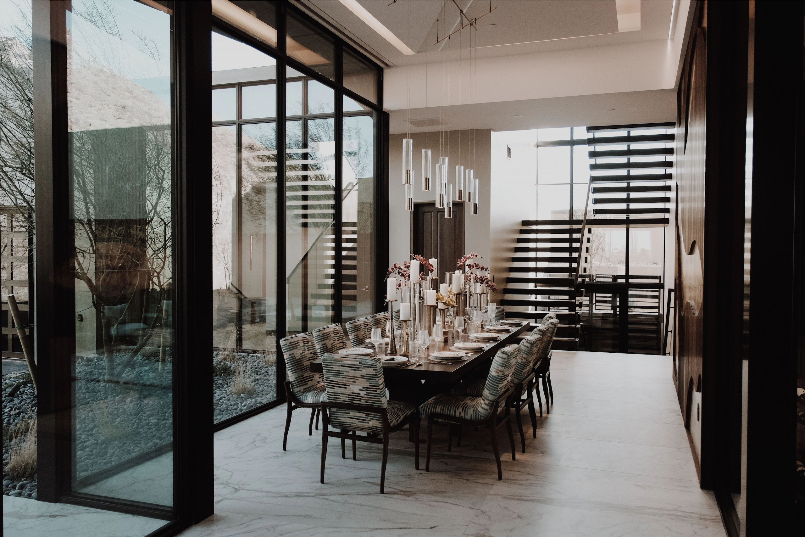 Glass walls open on a dining room with a cantilever stair rising behind it