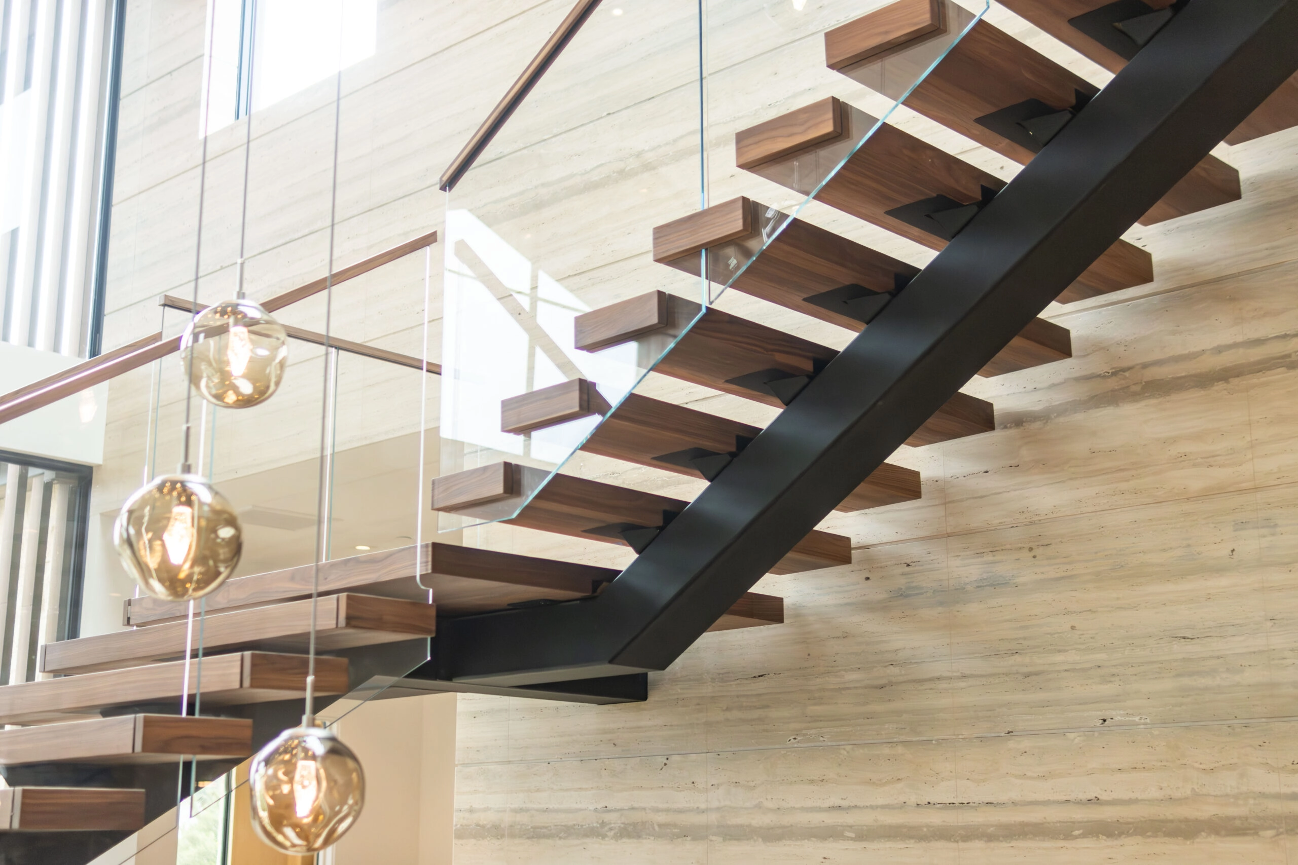 An extra-wide floating stair passes a row of amber globe pendants
