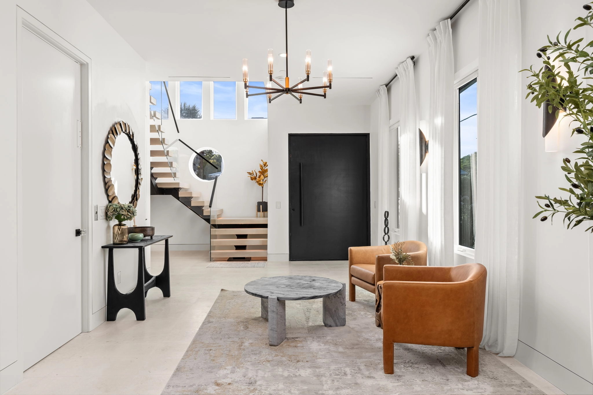 A floating stair and glass railing sit beyond leather chairs in a pale room