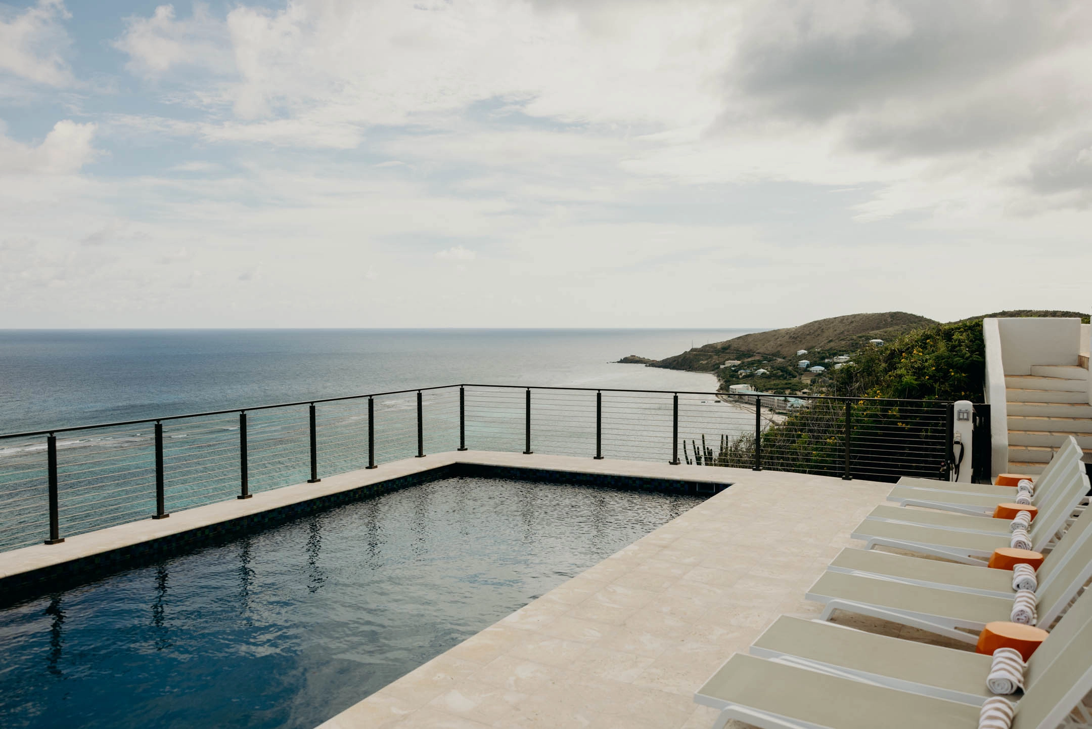 Rod infill in black posts runs beside a cliff-edge pool facing the ocean