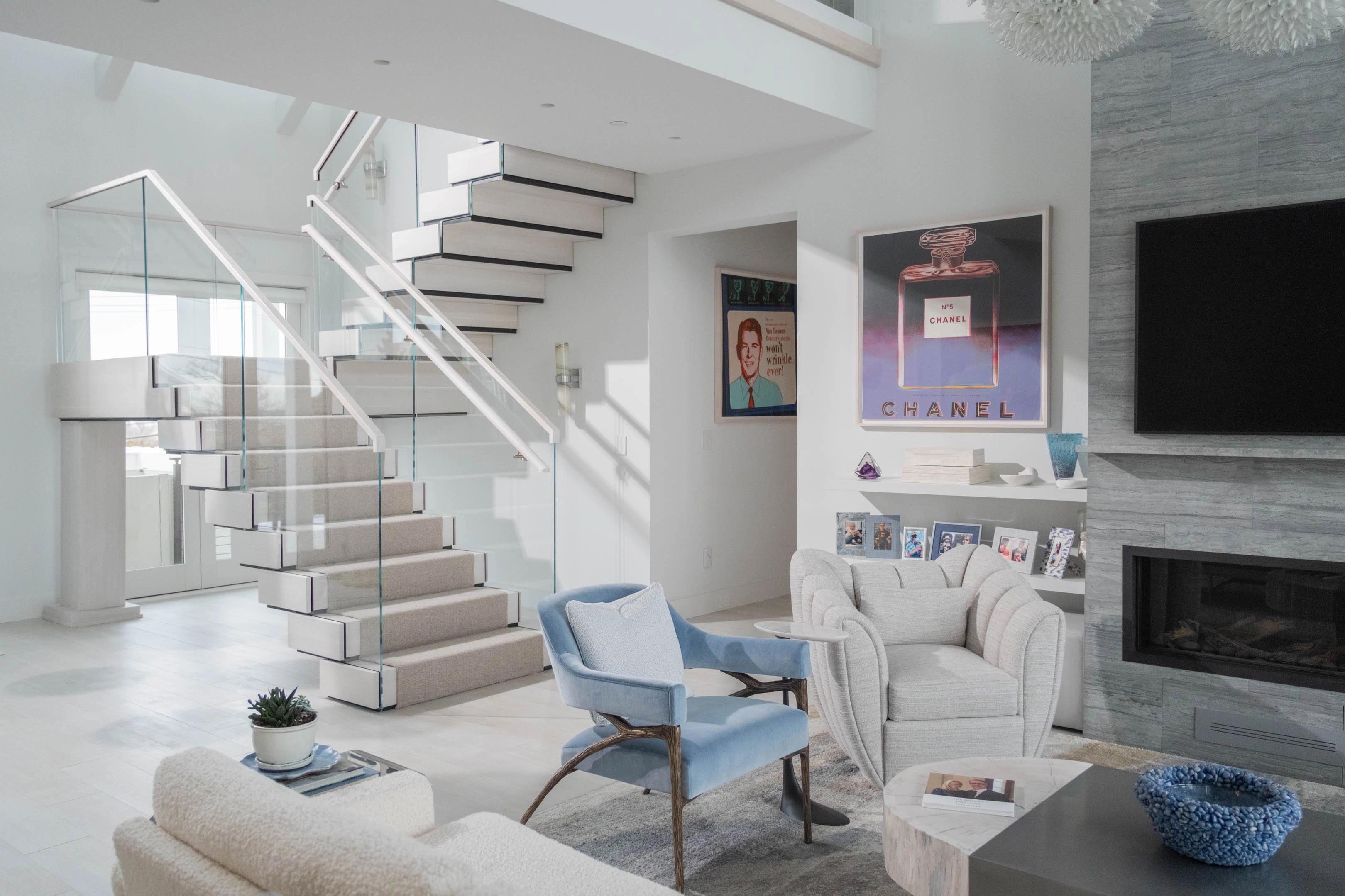 Stacked treads and glass railing rise beside a white living room hearth