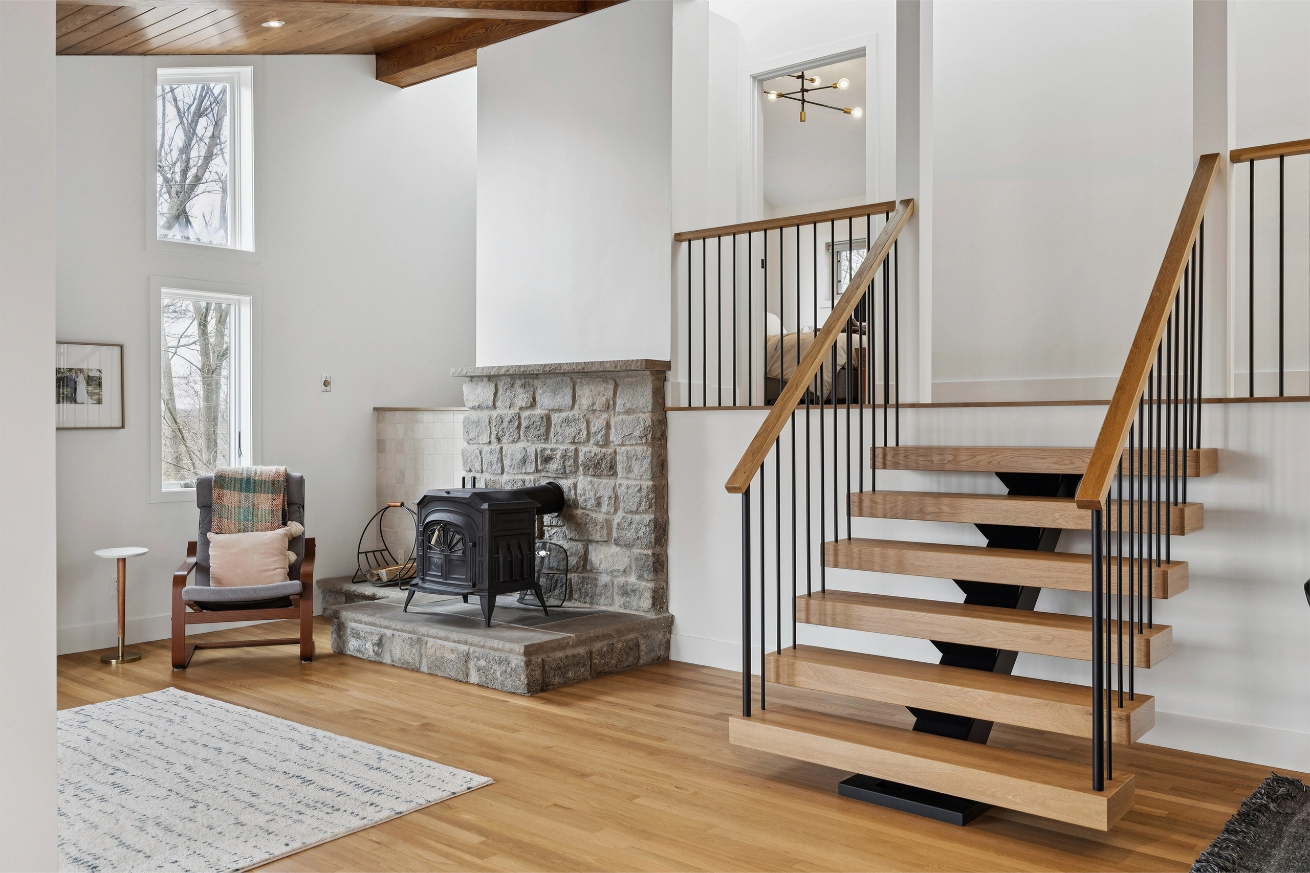 Floating treads and slim balusters rise beside a stone hearth and seating