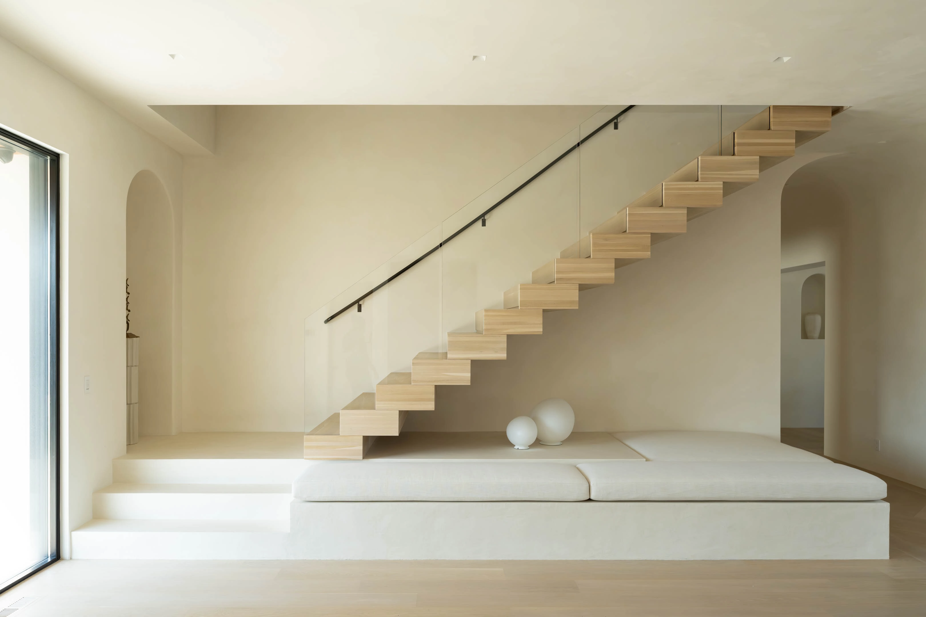 Pale plaster shapes a quiet room where a slim floating stair climbs one wall