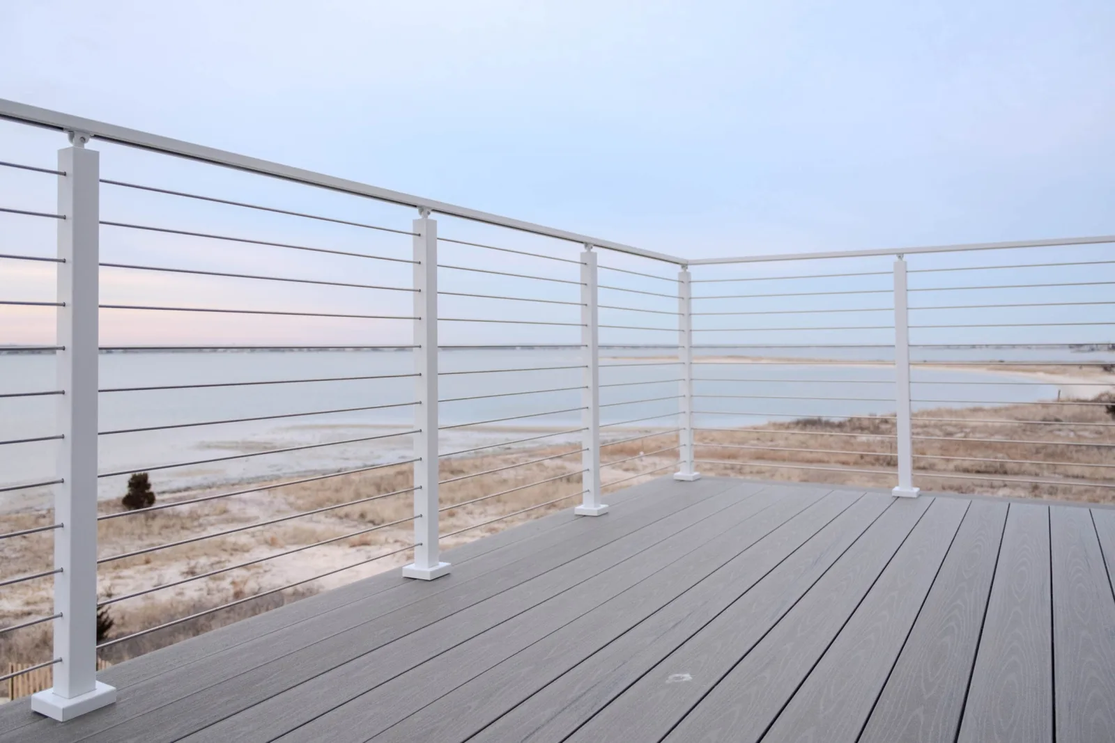 White posts carry rod infill along a coastal deck under a pale evening sky