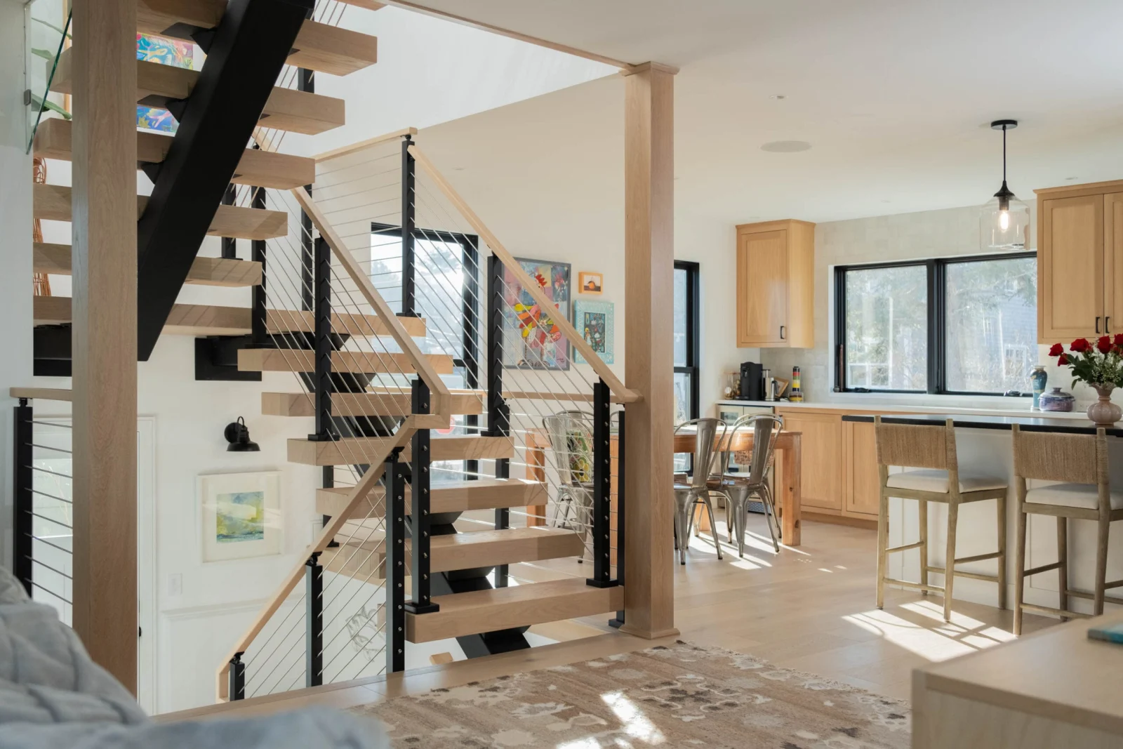 Rod railing and a wood handrail follow a floating stair beside an open kitchen