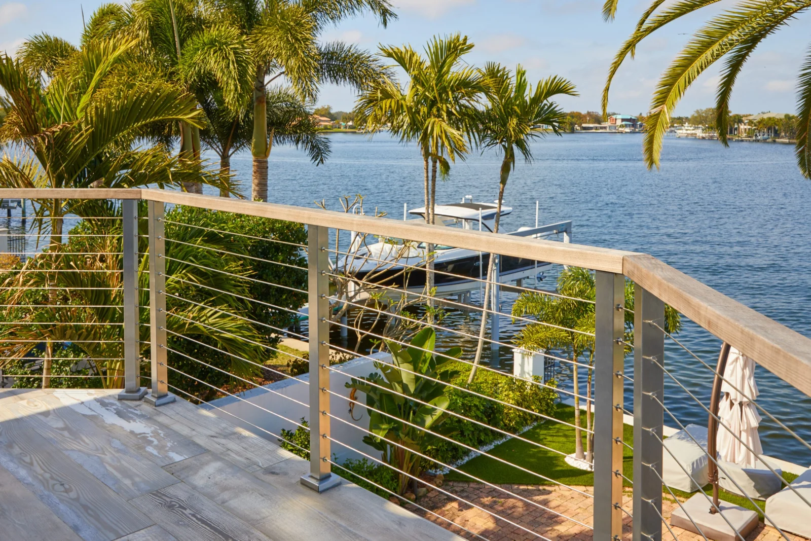 Cable railing borders a waterfront deck lined with palms on a canal
