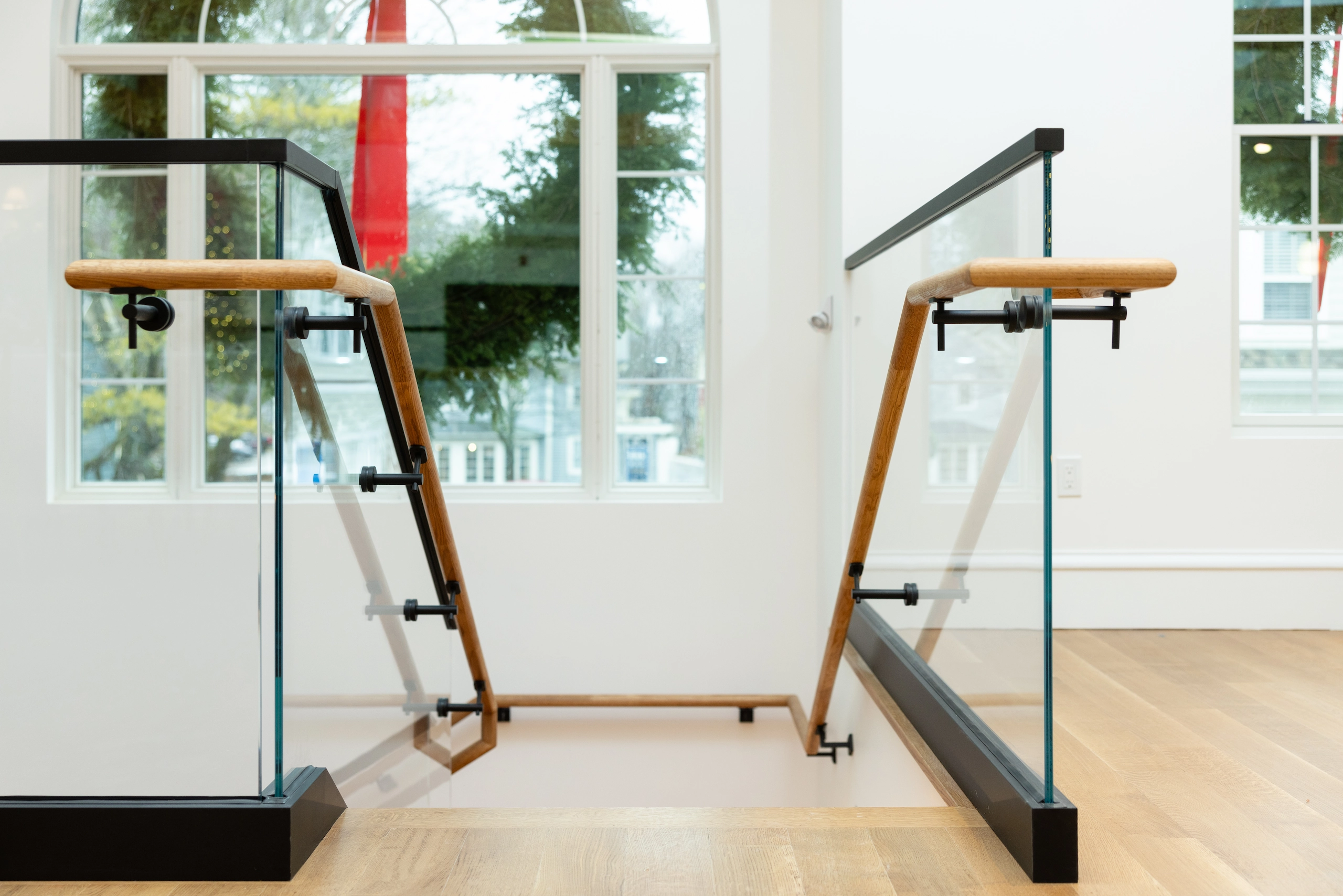 A continuous wood handrail turns with glass panels at a commercial entry