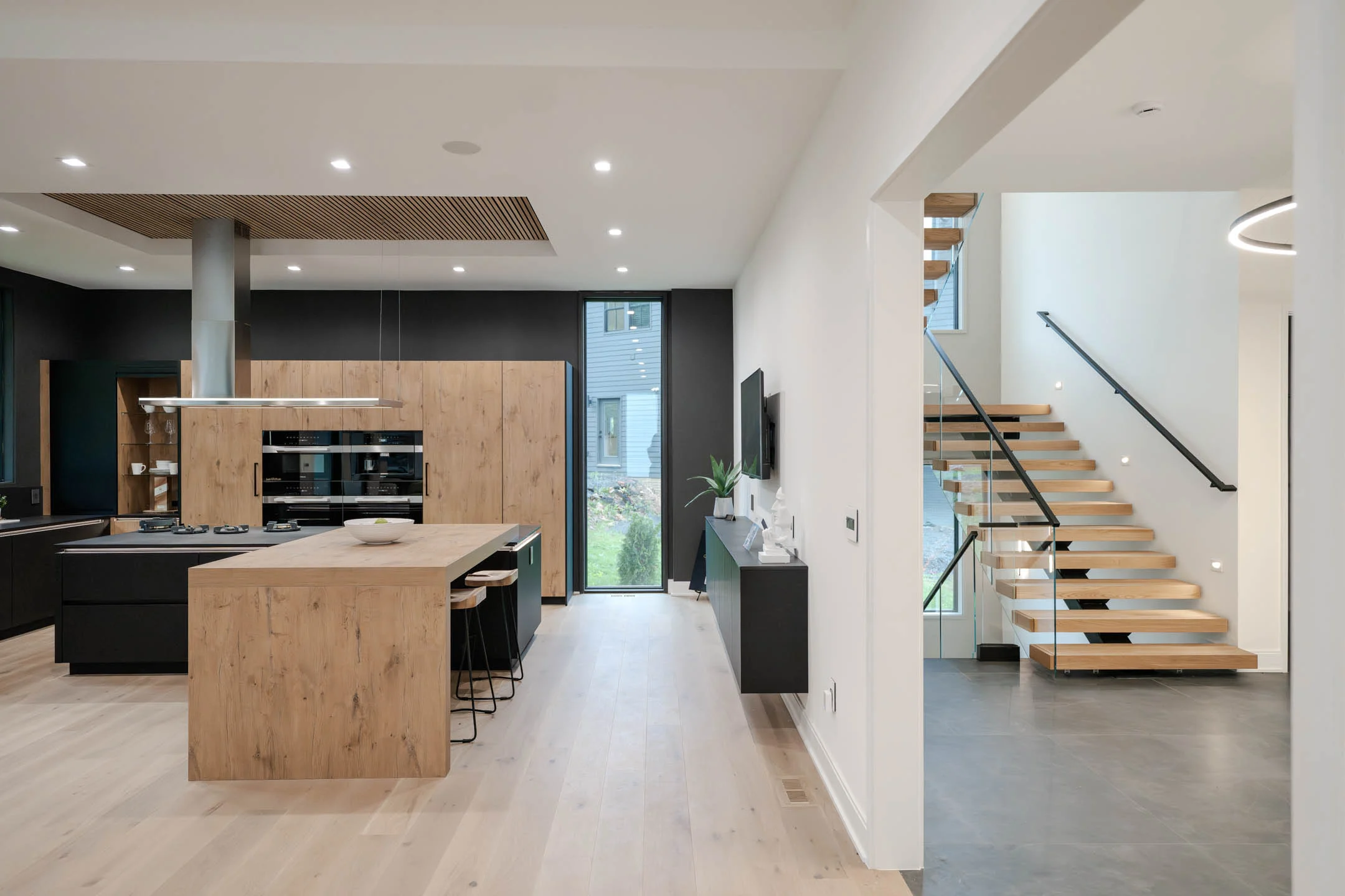 An open kitchen leads to a floating stair rising behind a glass panel