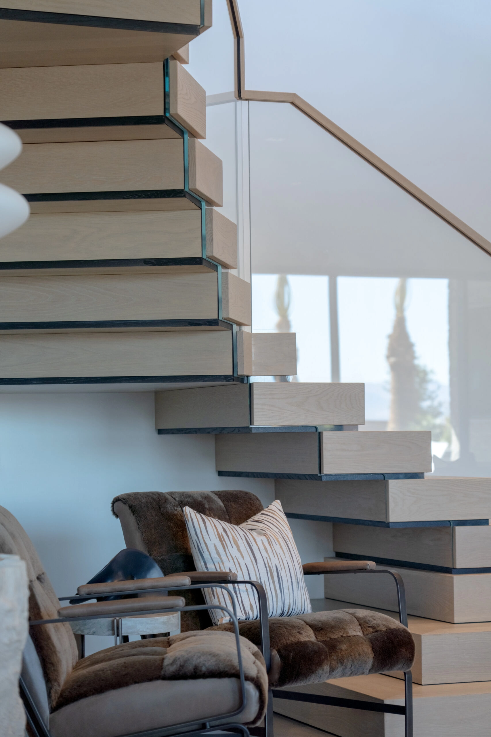 Stacked treads and glass railing pass above a leather-and-hide armchair
