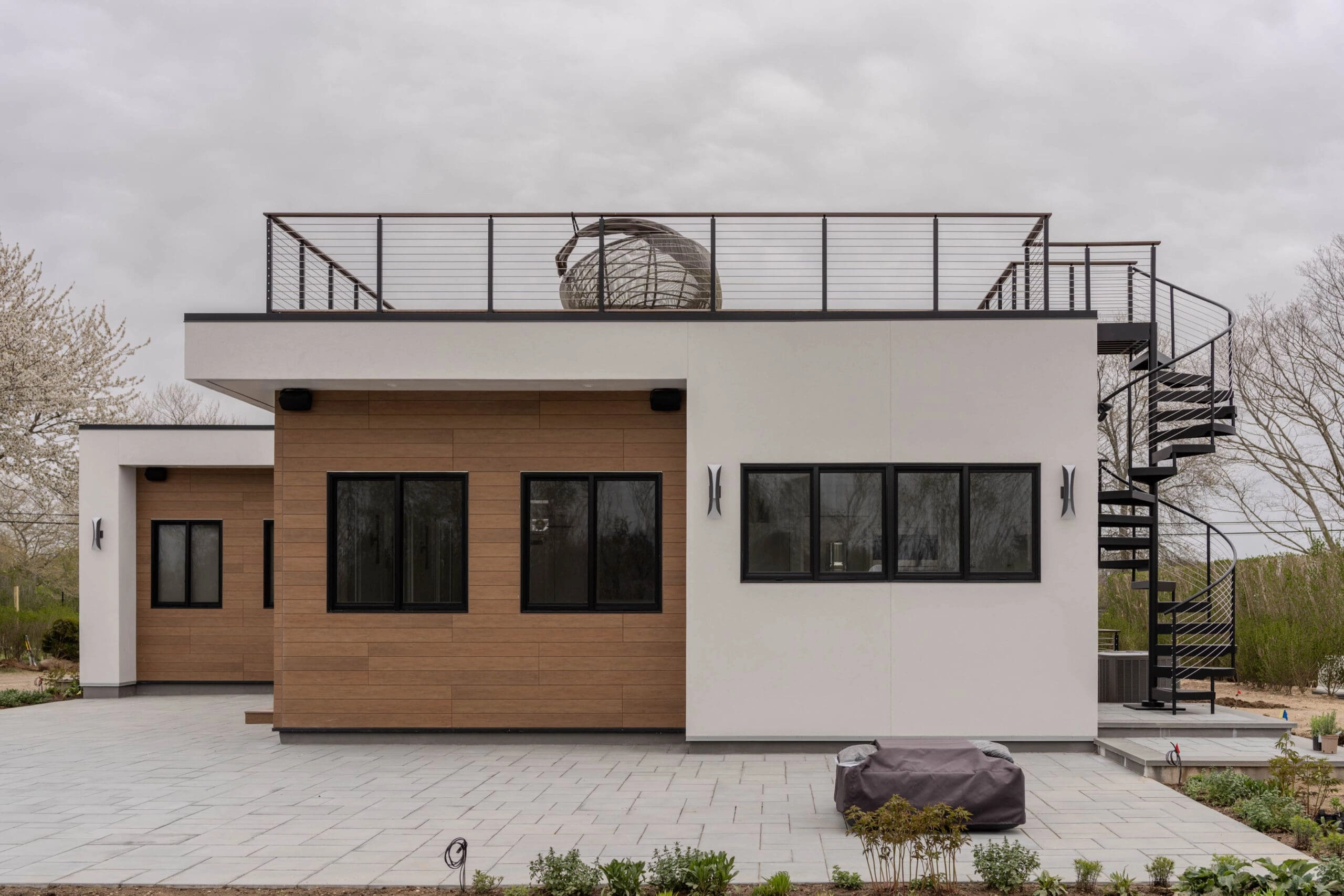 A black spiral stair climbs to a rooftop deck on a white and wood exterior