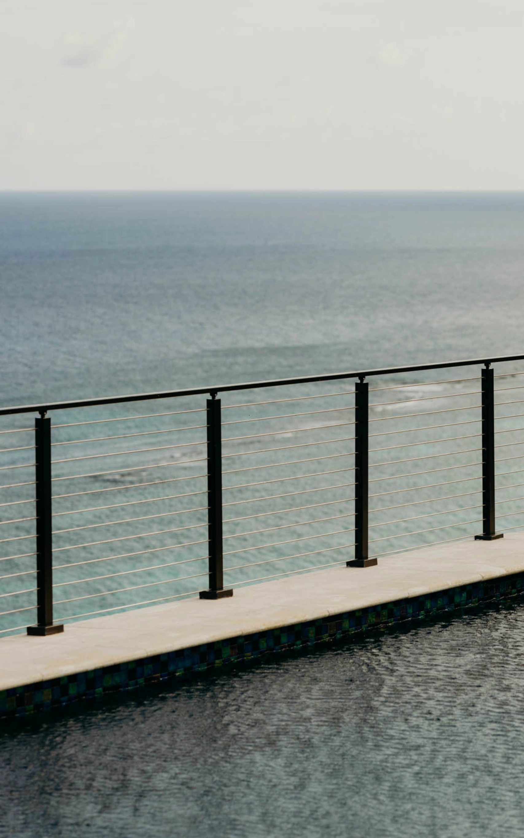 Black posts carry rod infill along a cliff-edge terrace above the ocean