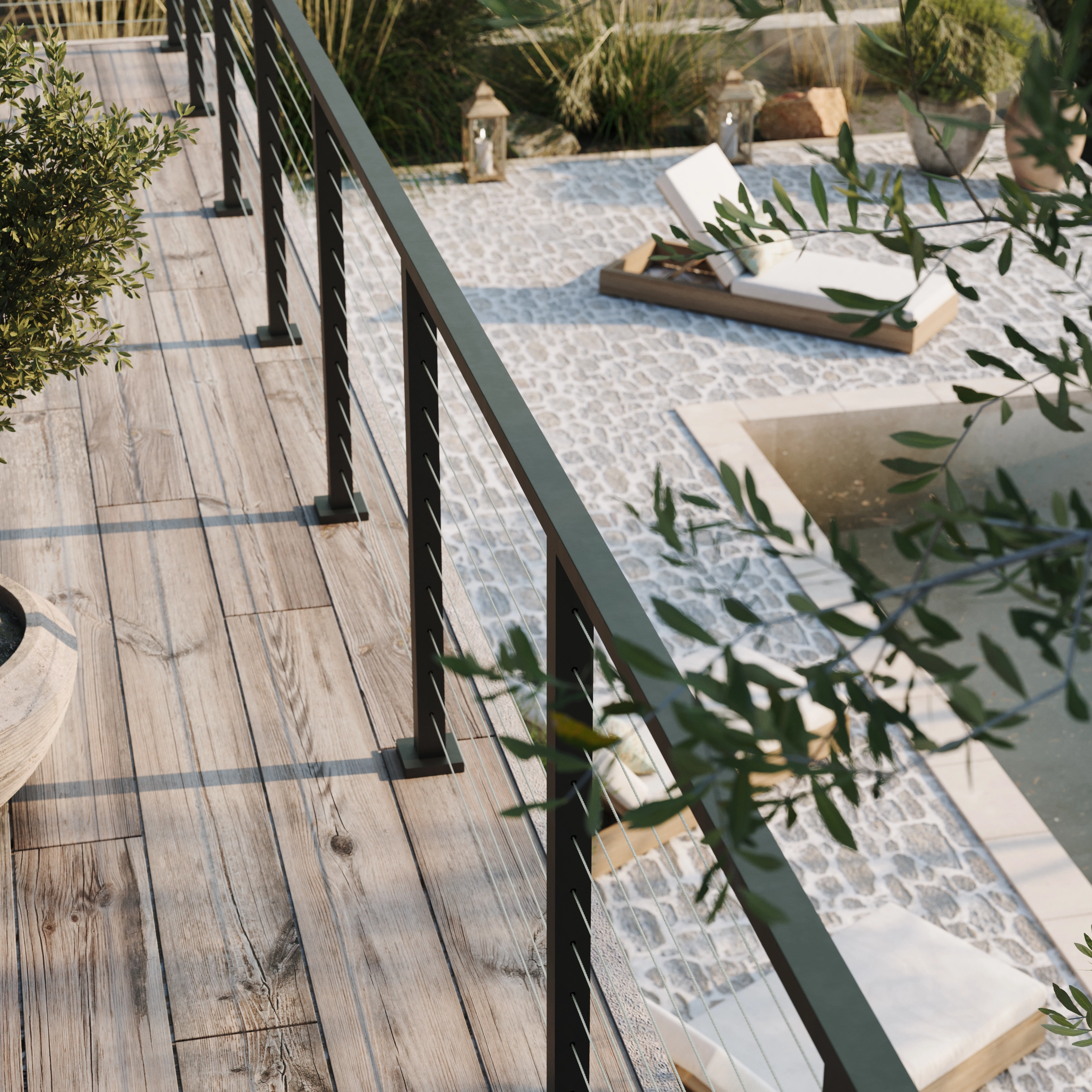 Cable railing runs along a deck overlooking a gravel courtyard and olive trees