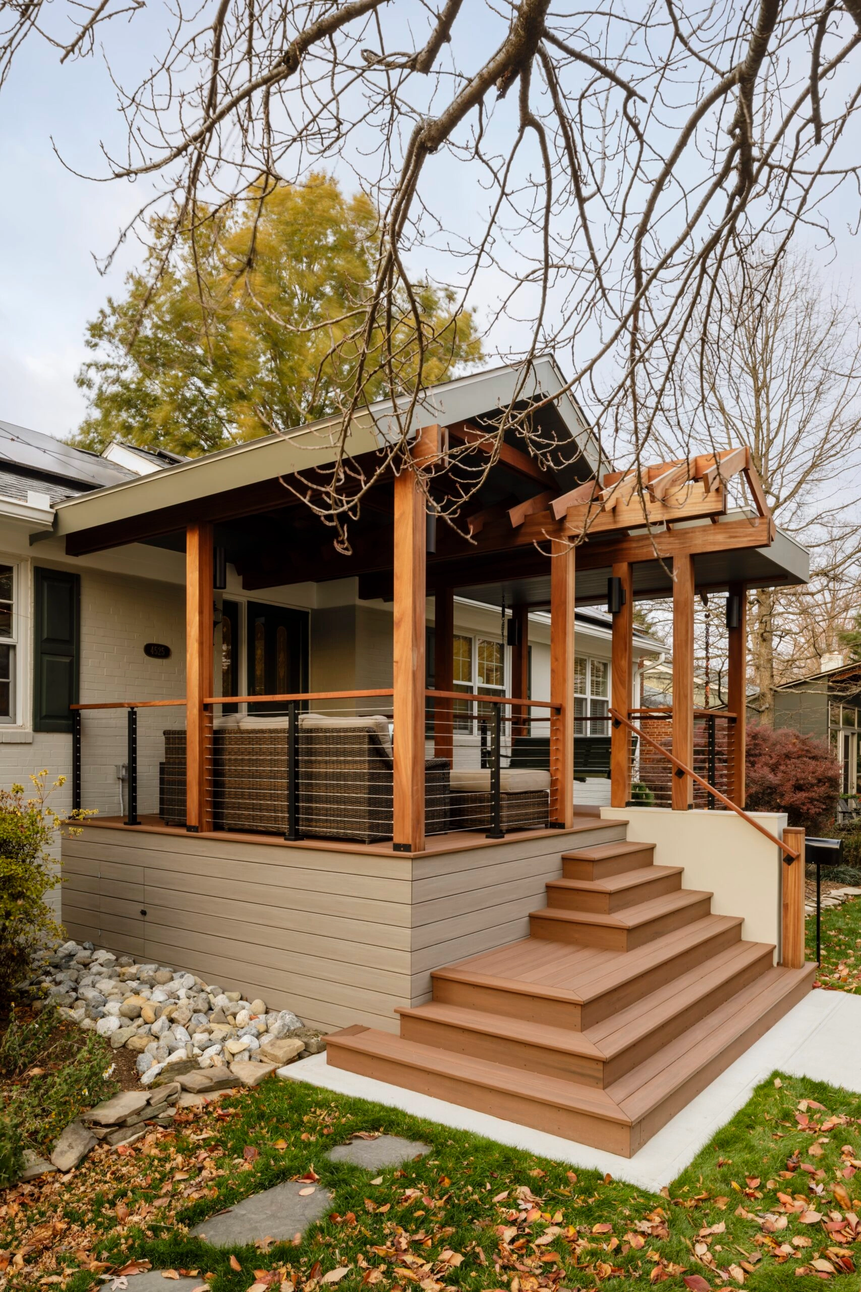 Cable railing follows a porch and its entry steps under a timber-framed roof
