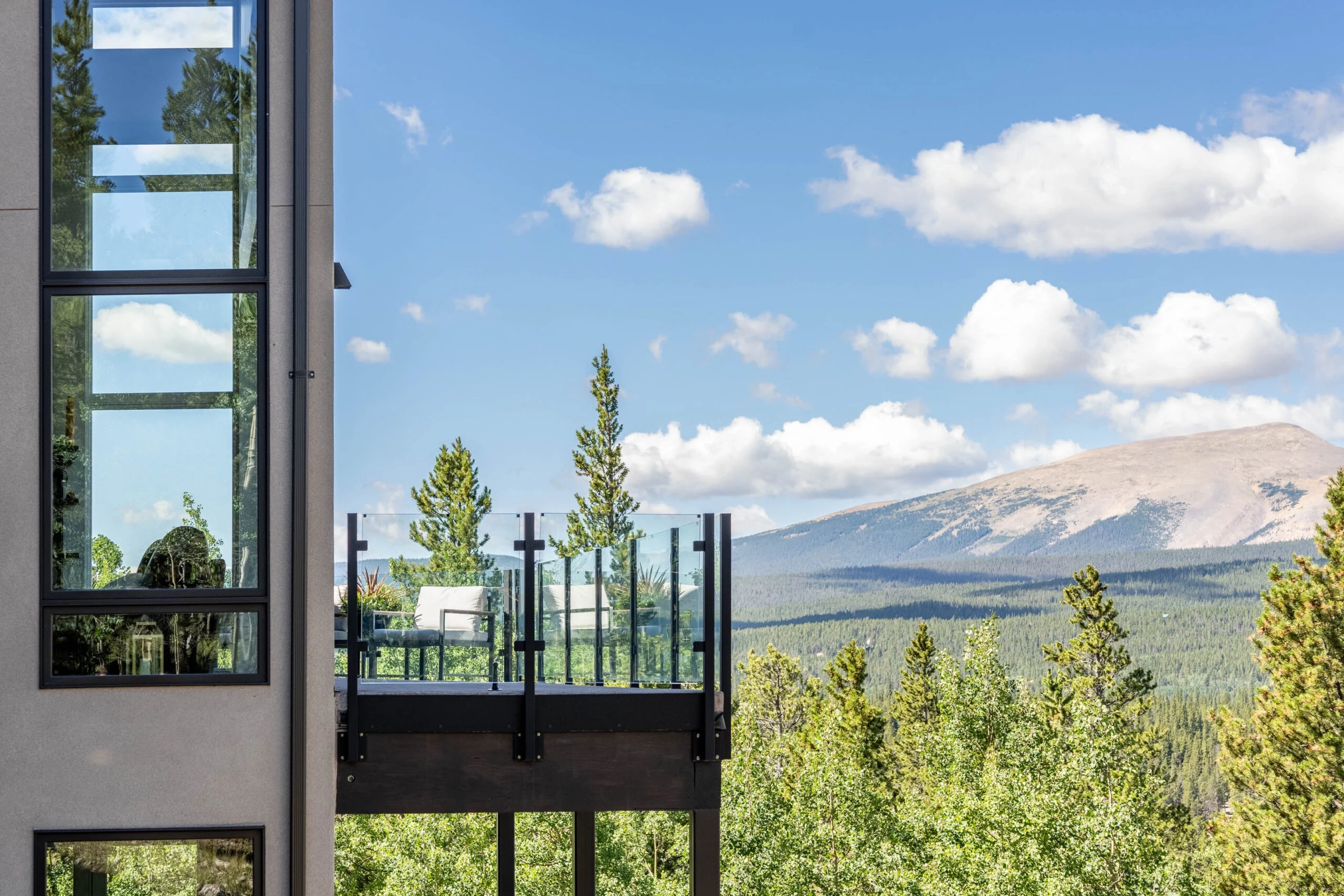 Black posts and glass open a balcony to a mountain range beyond the pines