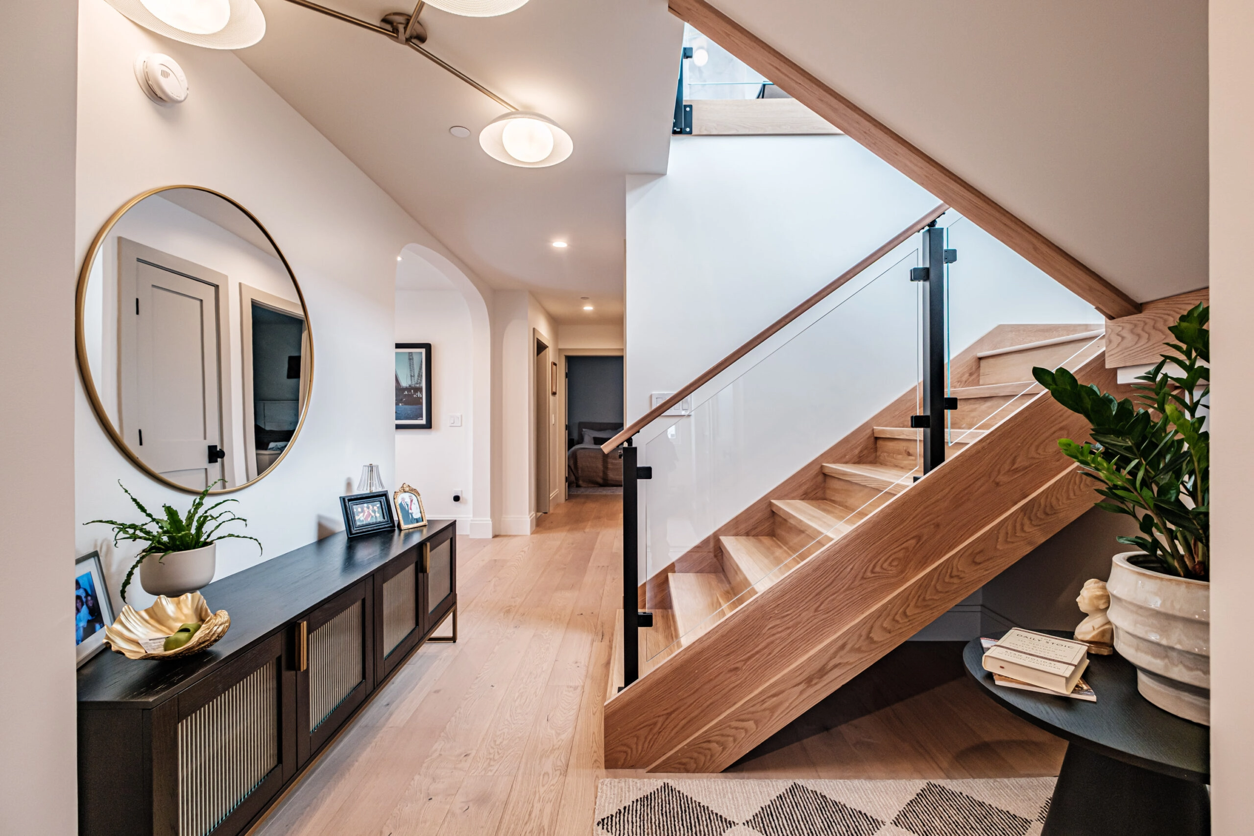 Glass panels in black posts edge a stair beside a hallway console and mirror